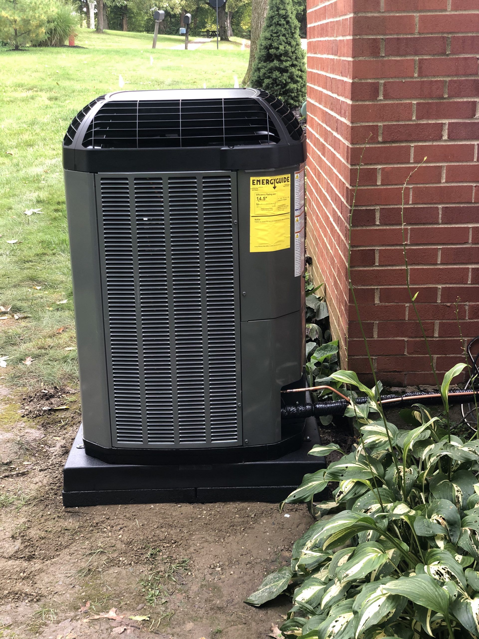 Air conditioning unit next to a brick wall and foliage outdoors.