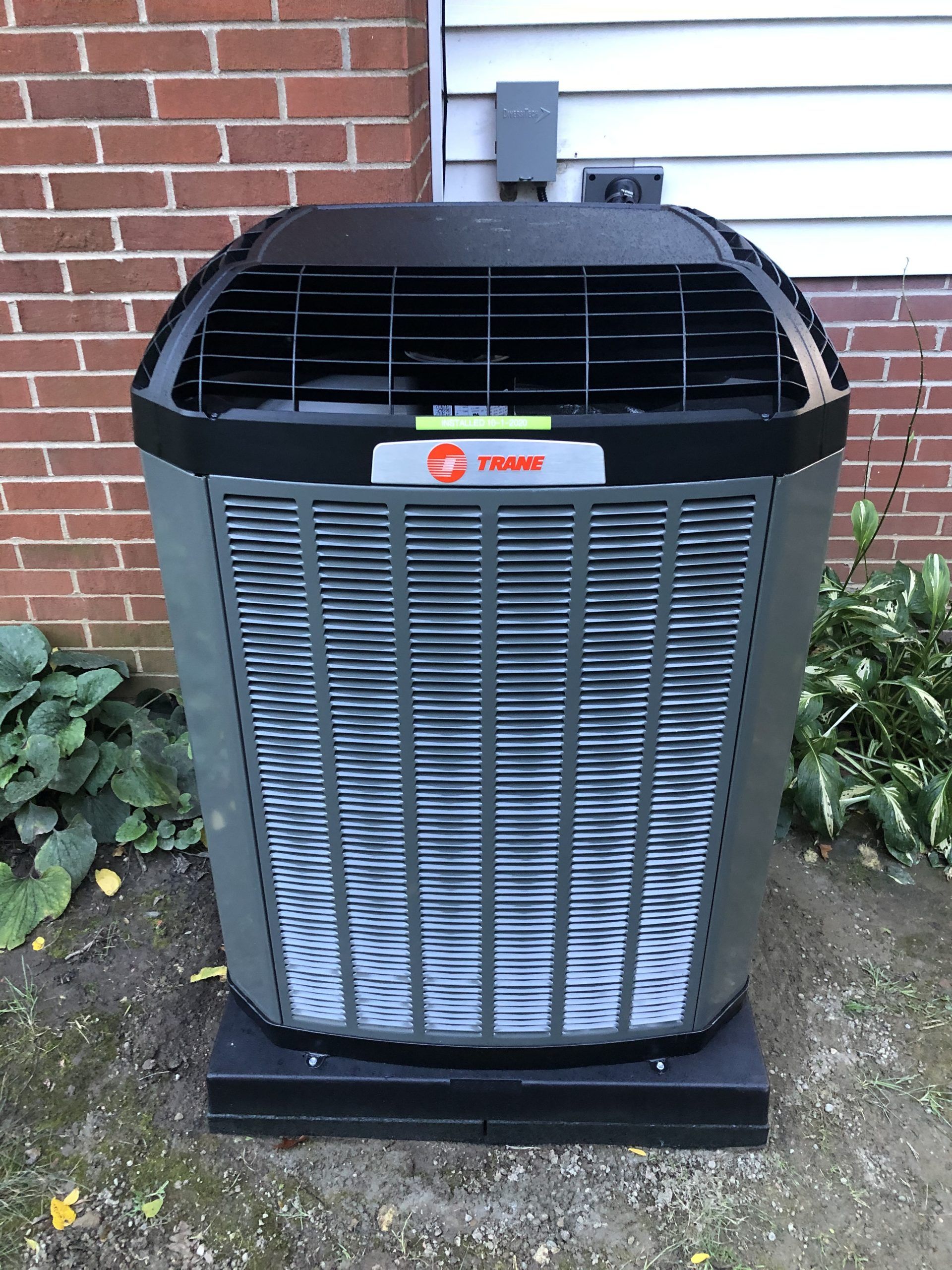 Trane air conditioning unit outside a brick building. Gray metal with black top and base.