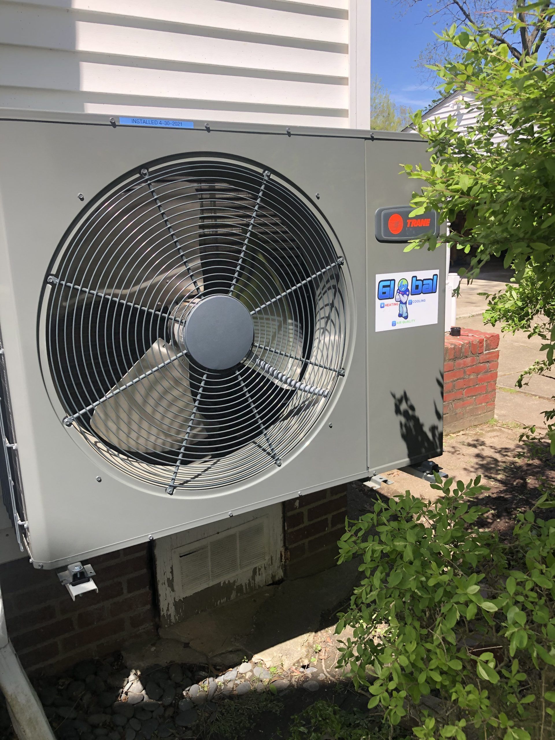 A Trane air conditioning unit installed outside a building on a brick base.