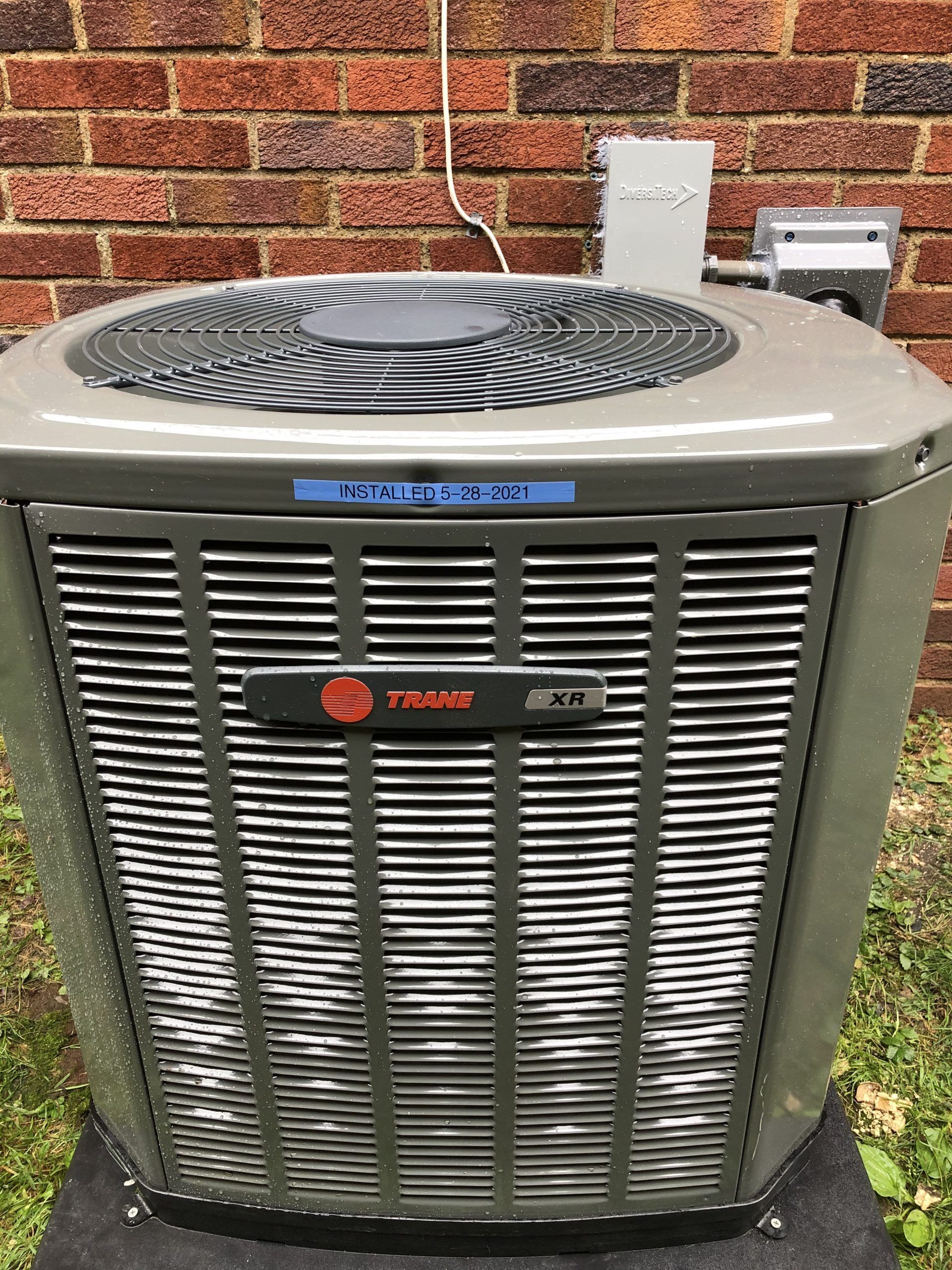 Gray Trane air conditioner unit in front of a brick wall.