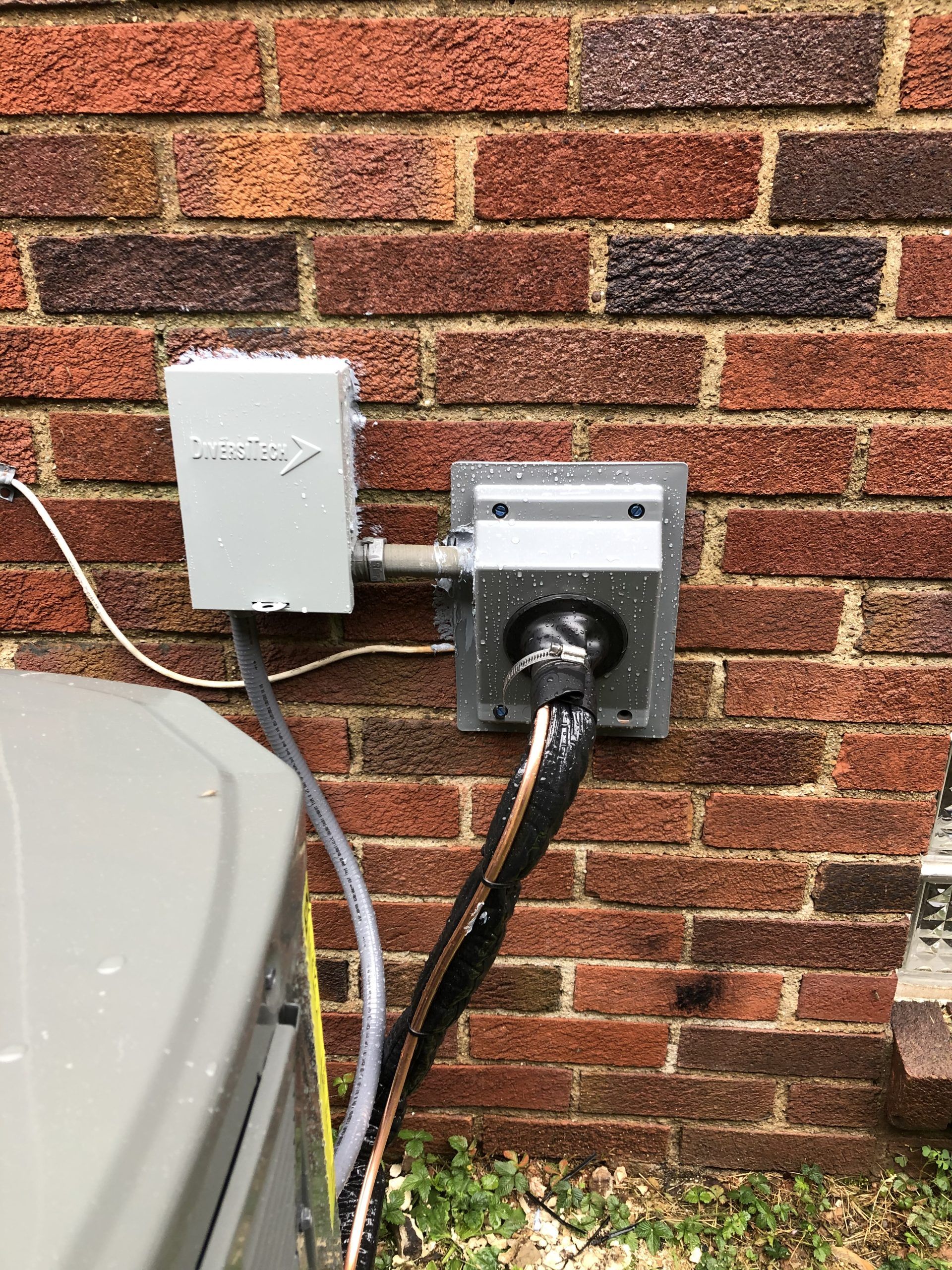 Electrical box and outlet on a brick wall, connected to an air conditioning unit.