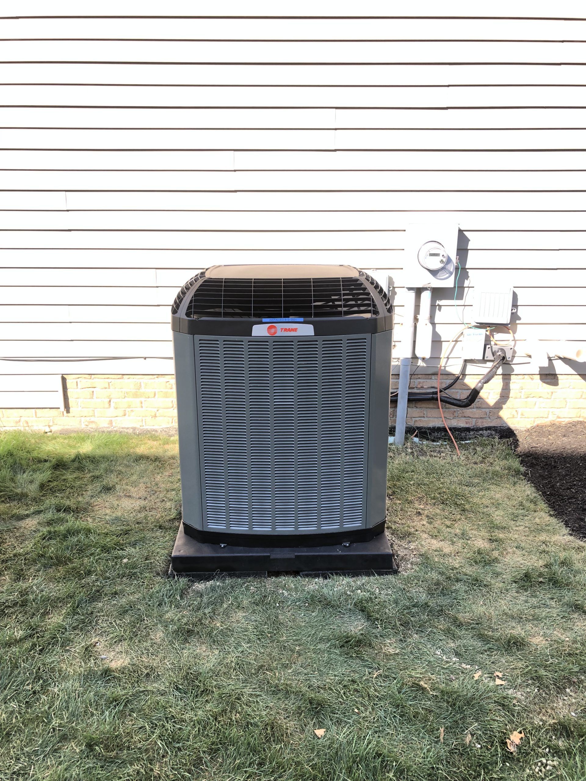 Air conditioning unit outside a white house on a grassy lawn.