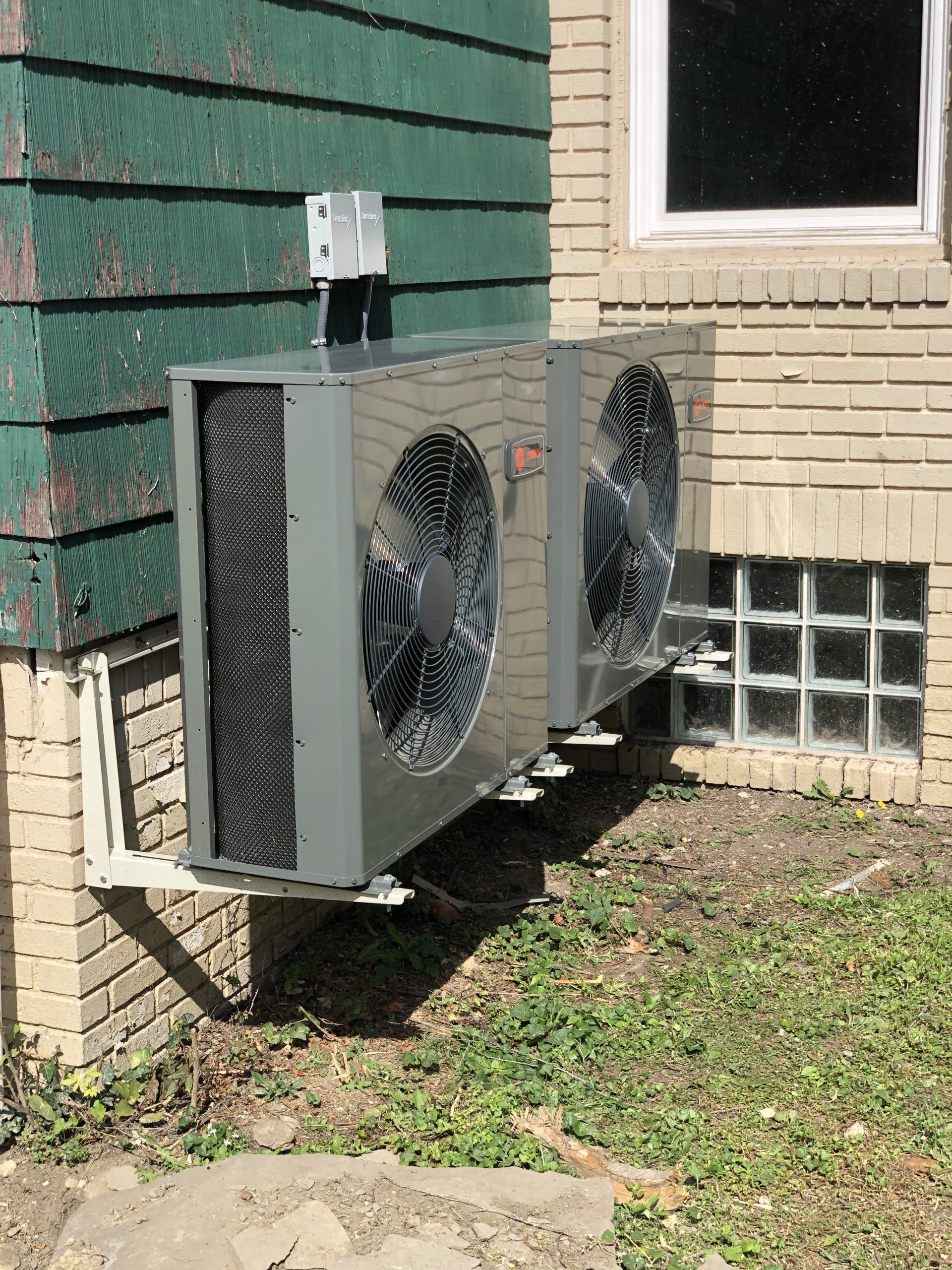 Wall-mounted HVAC unit outside a building, set against brick and siding.
