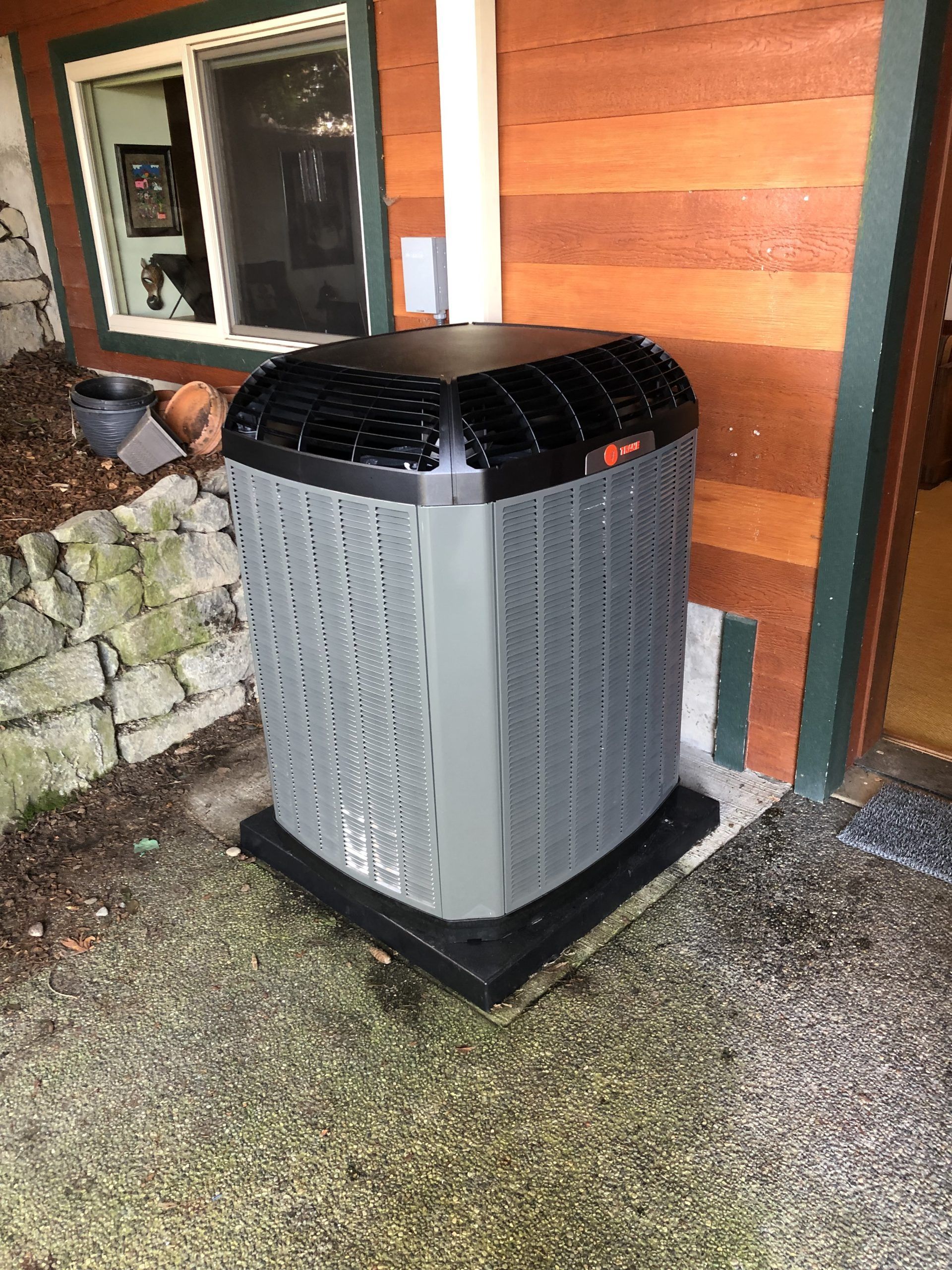 Gray and black air conditioning unit outside a building with brown siding.