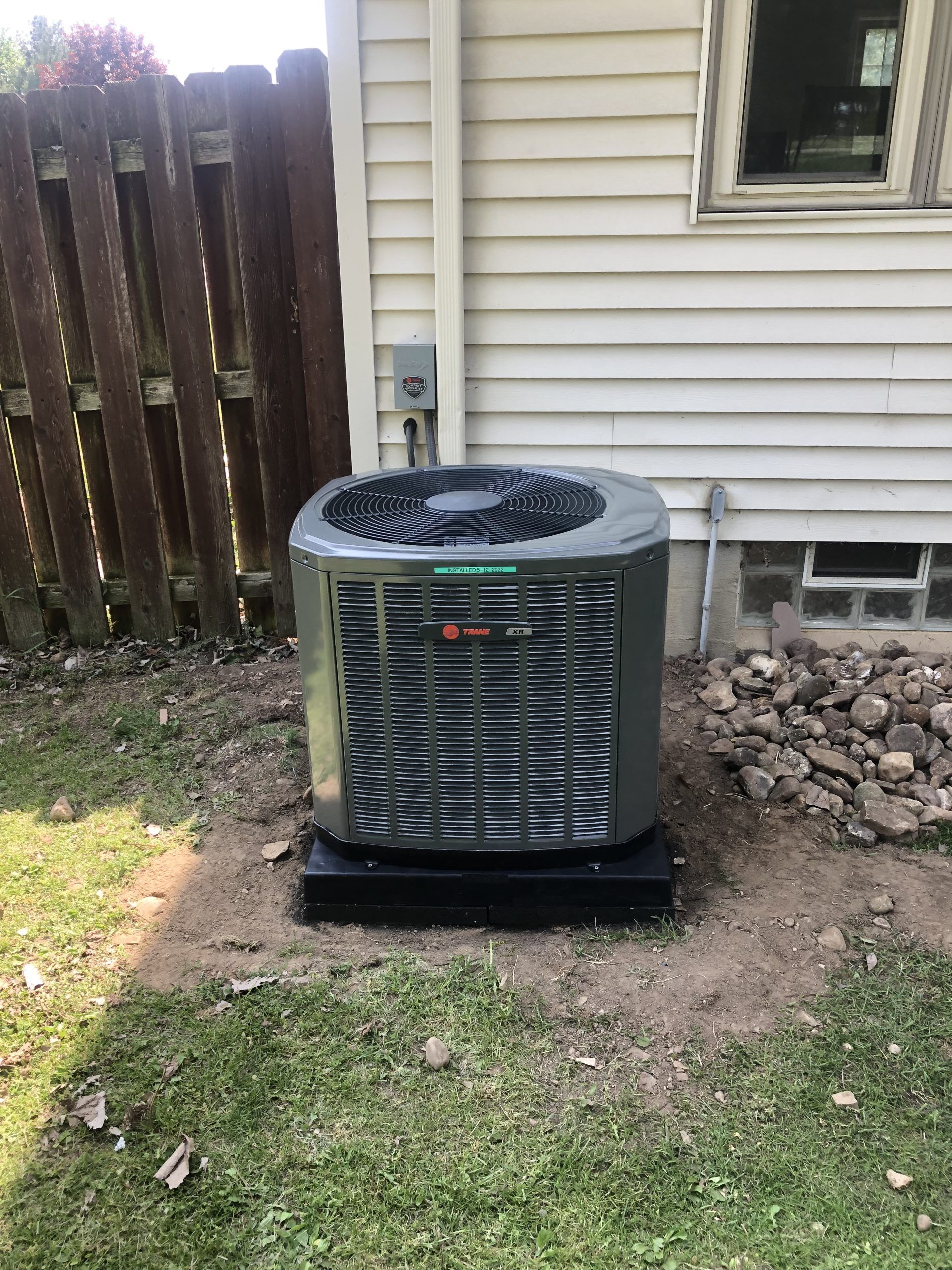 Air conditioning unit next to a white house with a brown fence.