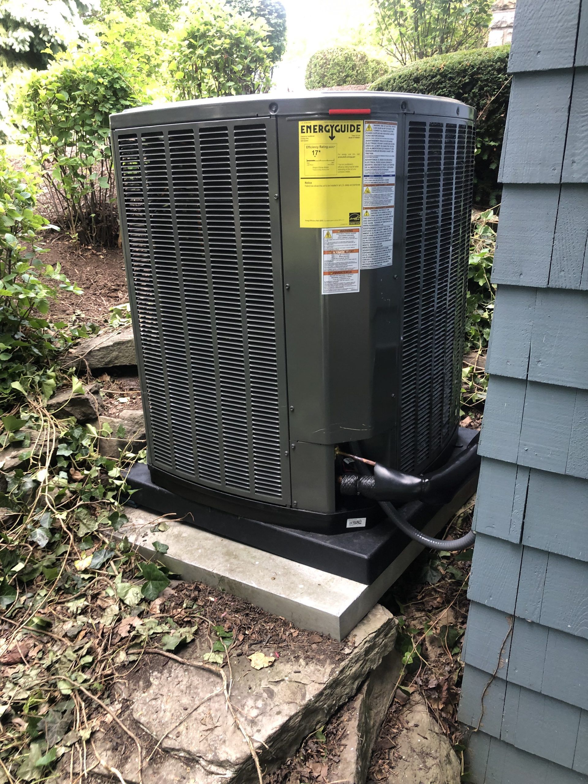Gray HVAC unit on a concrete base next to a blue house siding, outdoors.