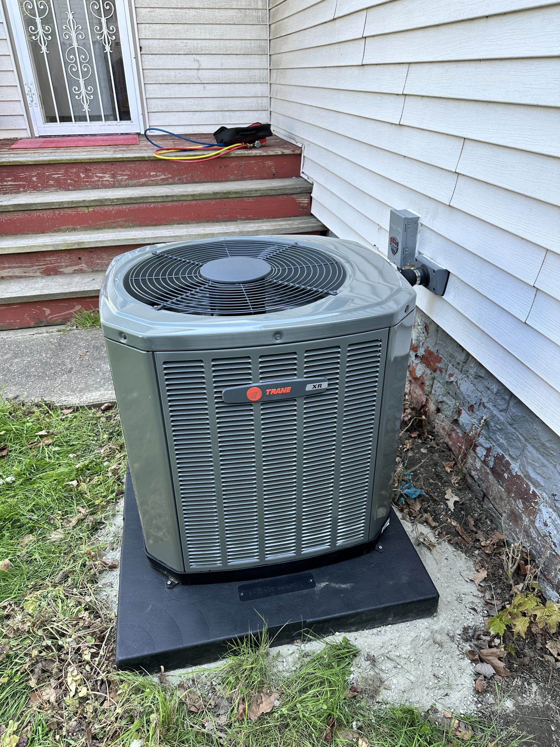 Gray Trane air conditioner unit near a white house with red steps.