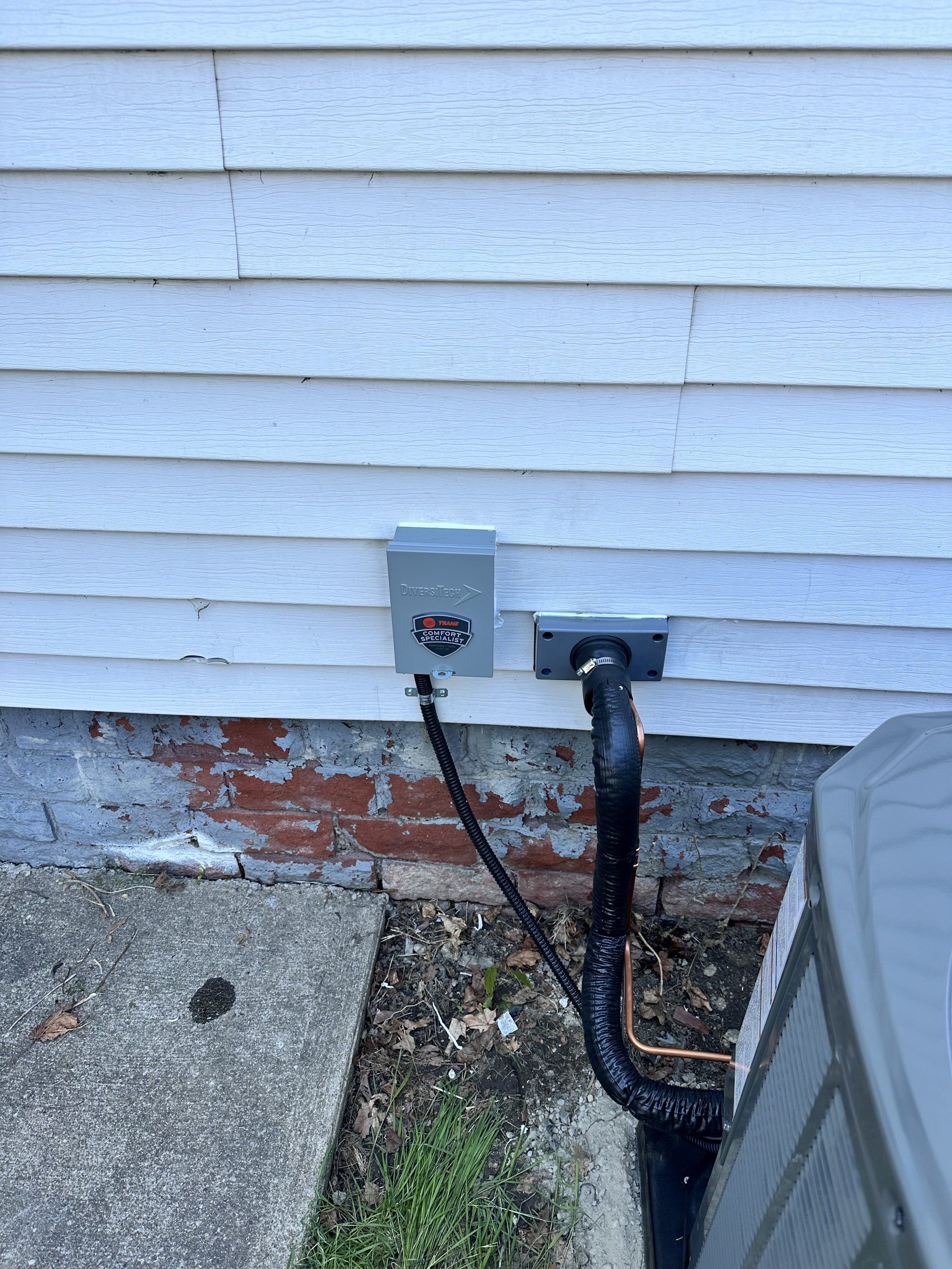 Exterior electrical box and AC unit against a white-sided house with a concrete slab.