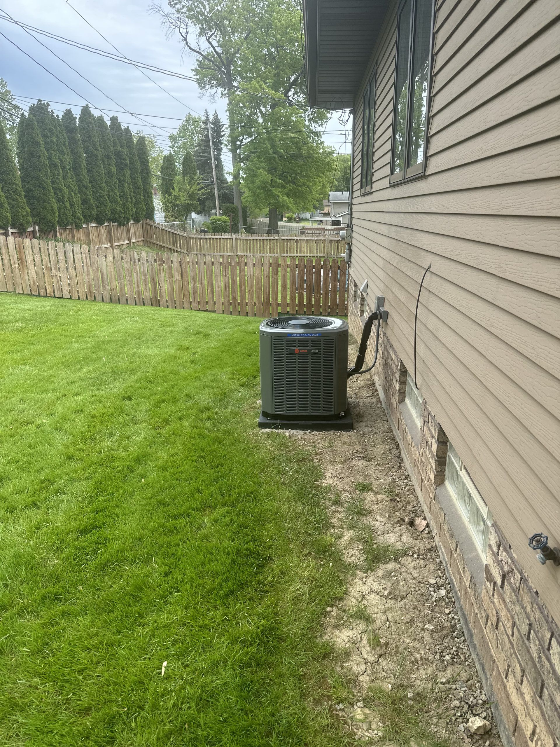 AC unit outside a house next to grassy lawn and a wooden fence.