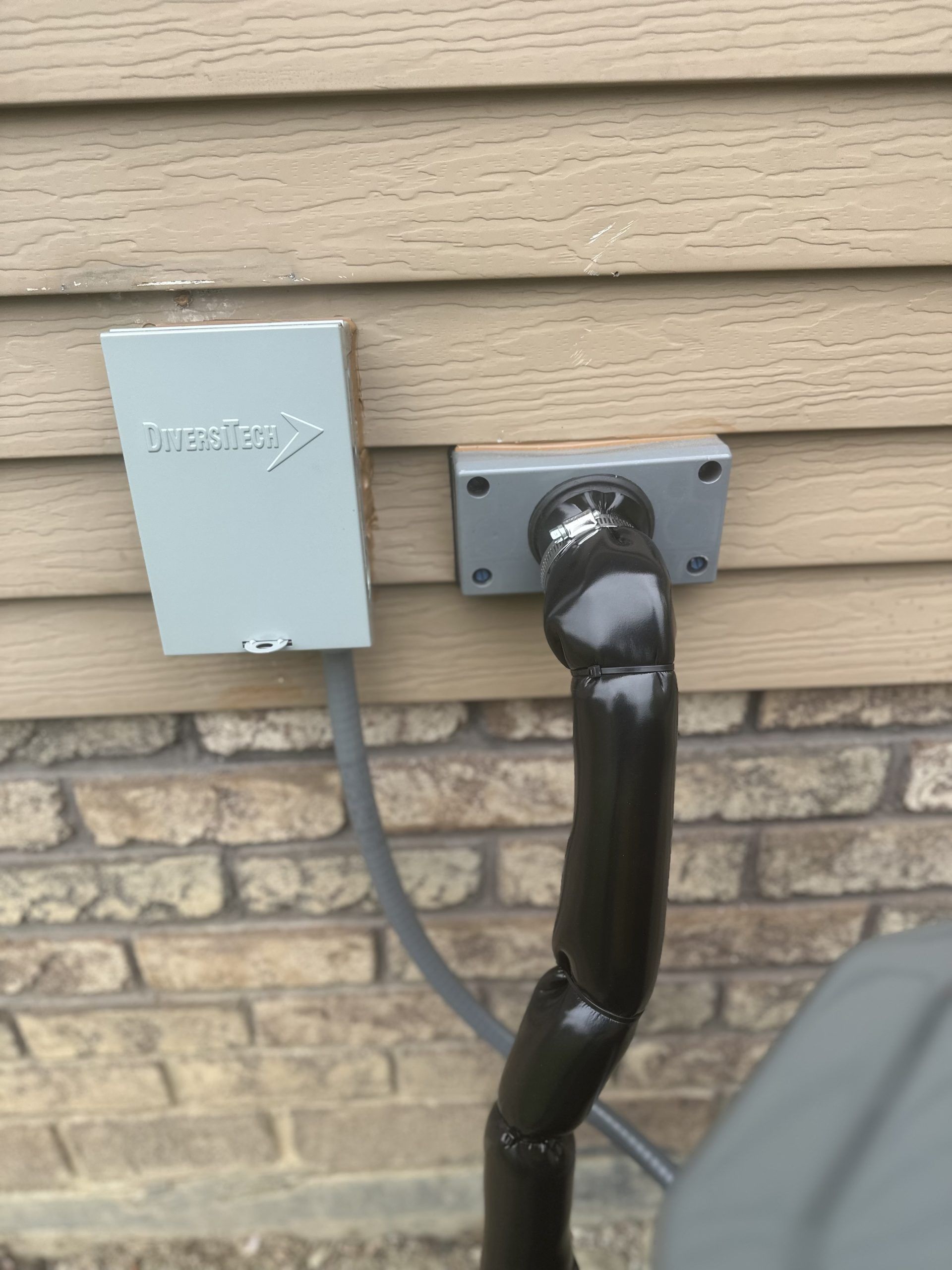 Outdoor electrical outlet and conduit on a brick and siding wall; a gray box is nearby.