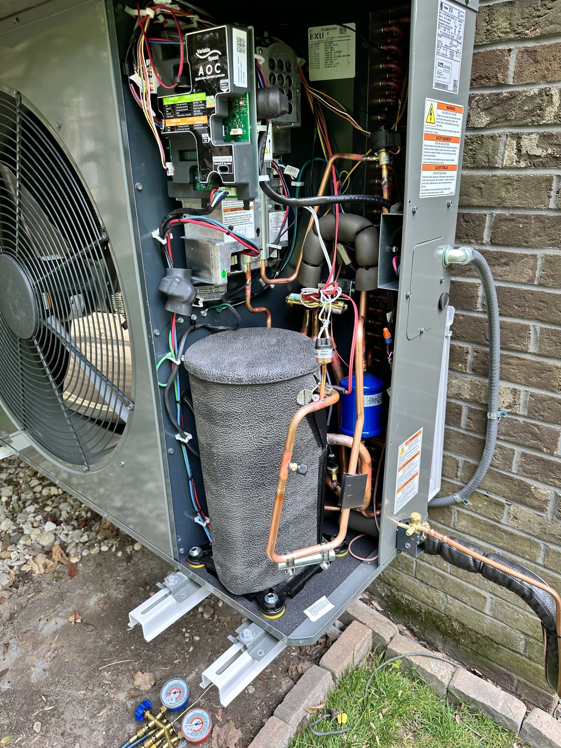 Open view of a heat pump unit's inner components; copper tubing, wires, and a cylinder-shaped component visible.