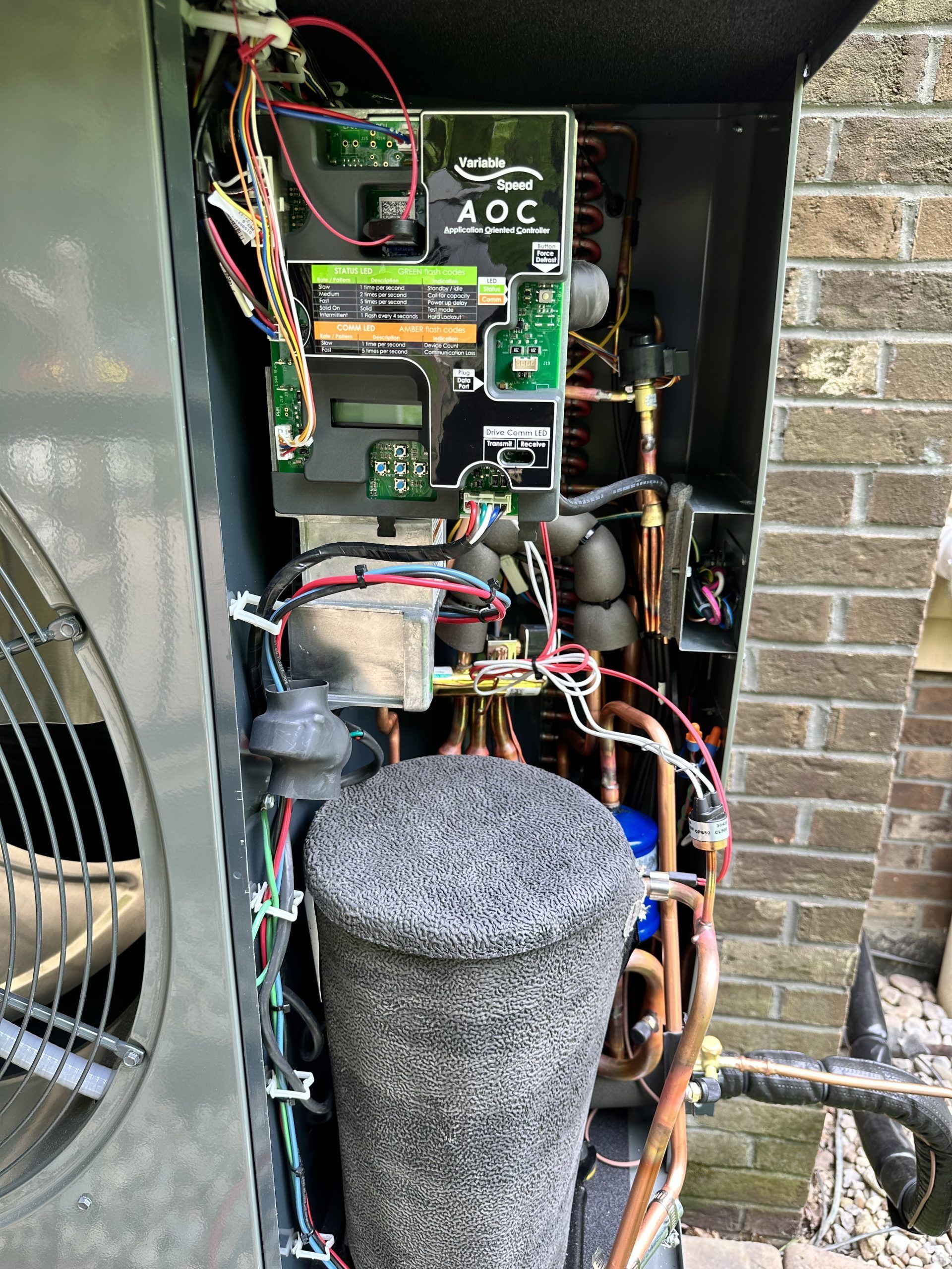 Open panel of a heat pump unit with electronic components, copper tubing, and insulated cylinder.
