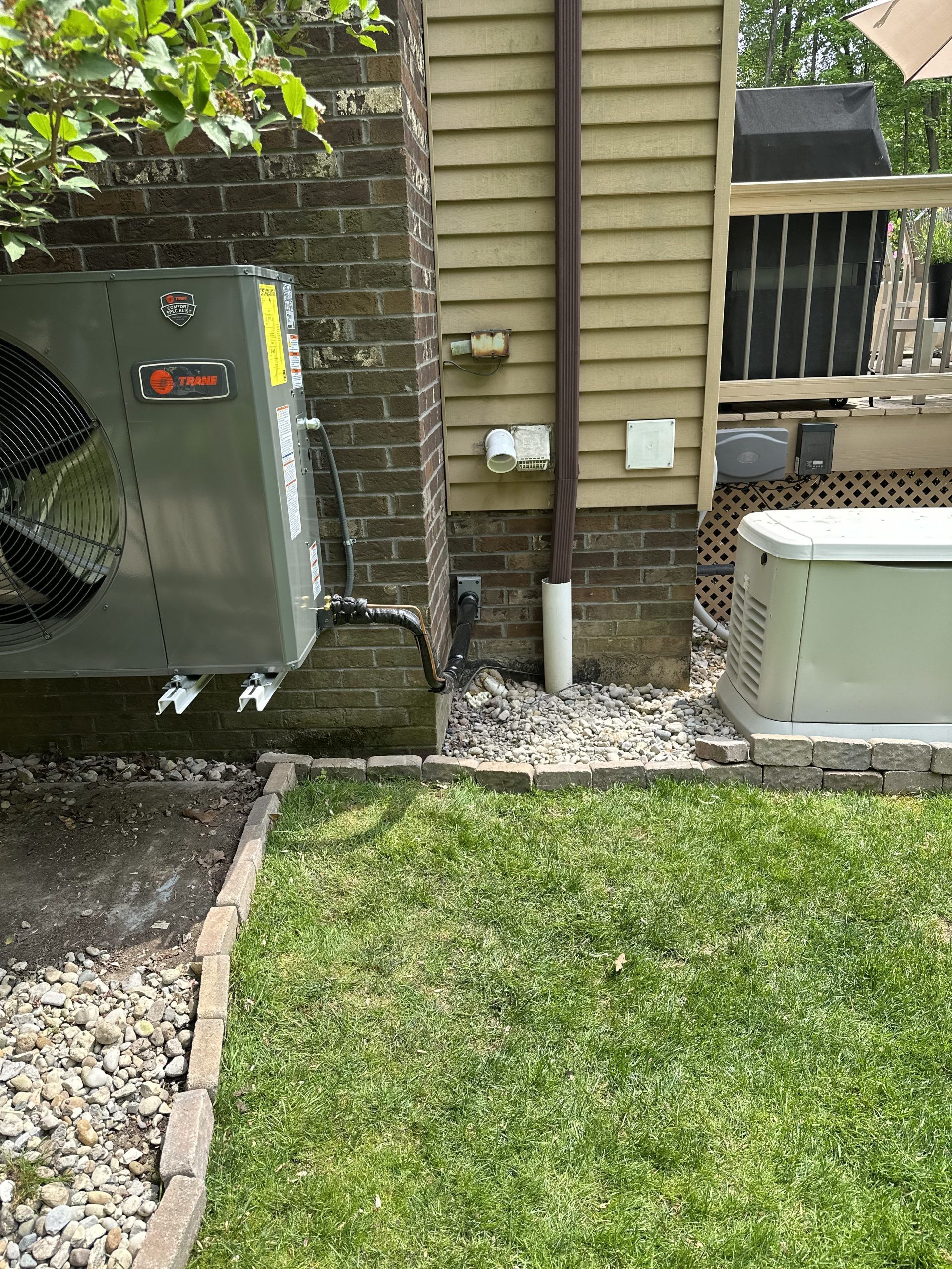 An outdoor view featuring an HVAC unit, brick wall, generator, and green lawn.