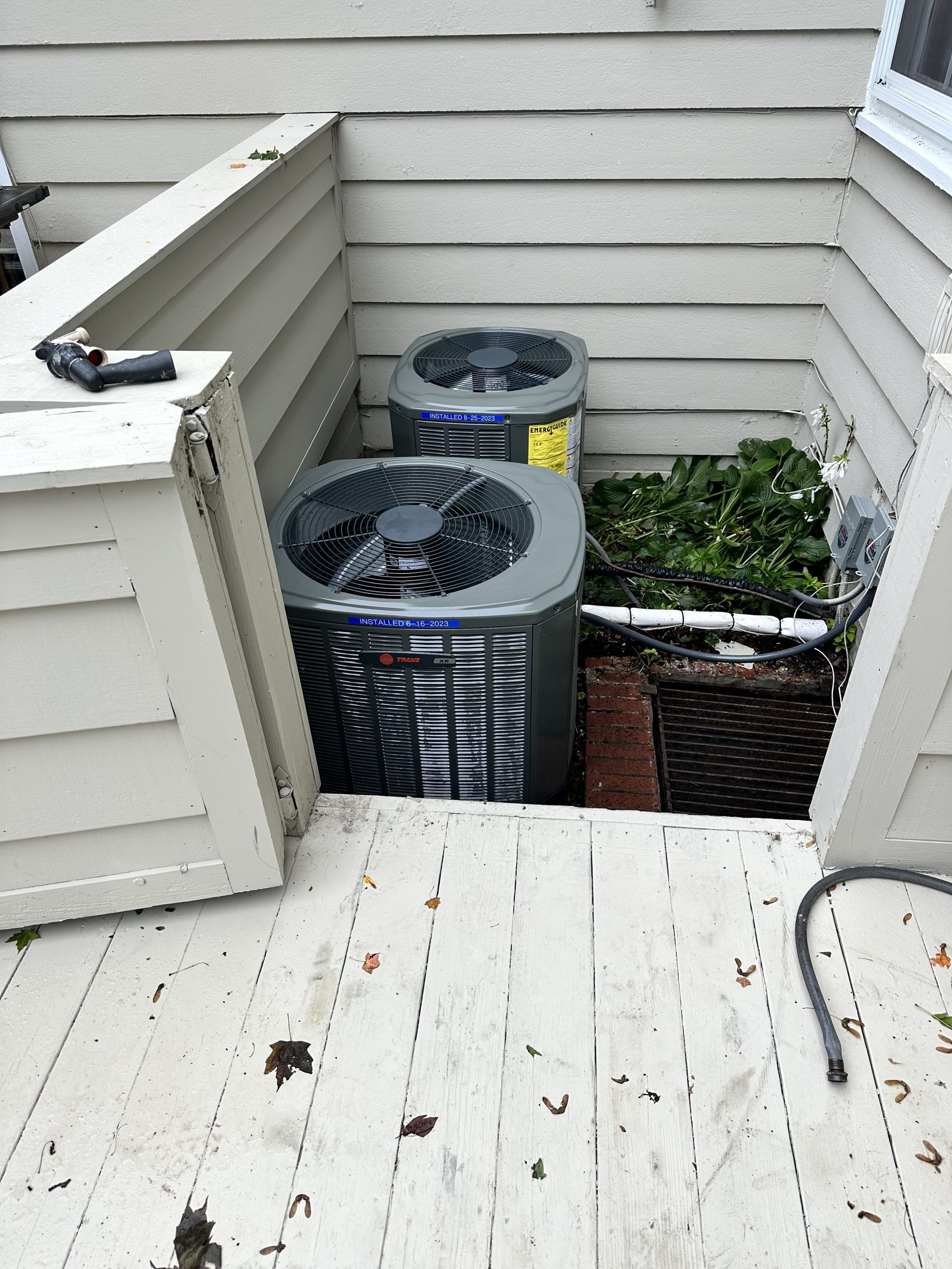 Two air conditioning units enclosed by a deck and siding; greenery in a basket.