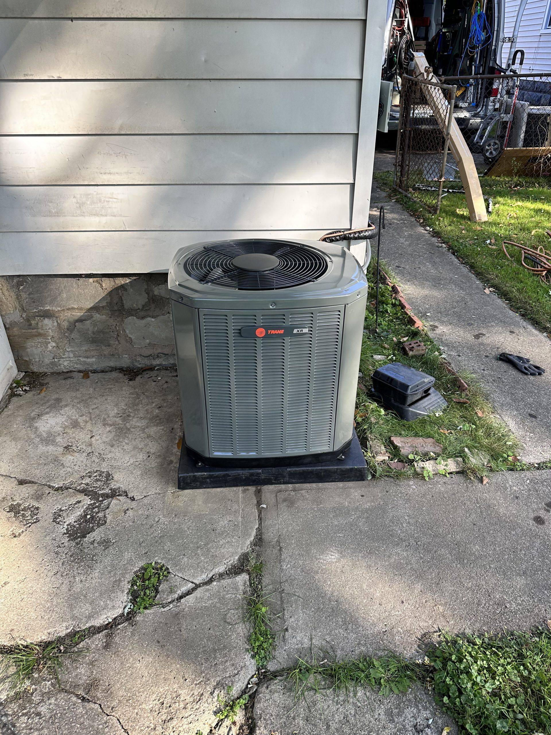 Air conditioning unit on a concrete pad next to a house with white siding.