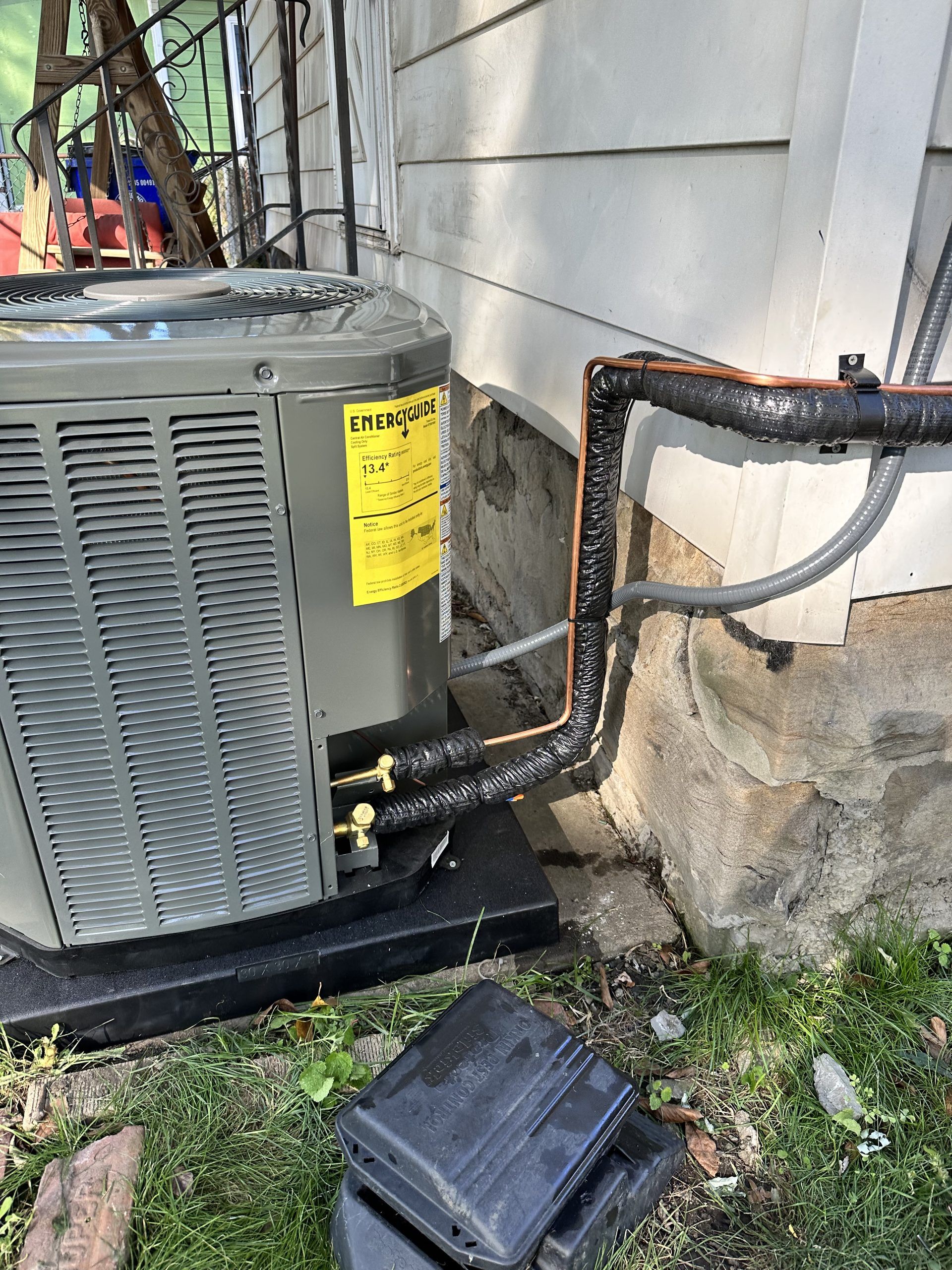 Air conditioner unit outside a house, with insulated pipes, sitting on a black base.