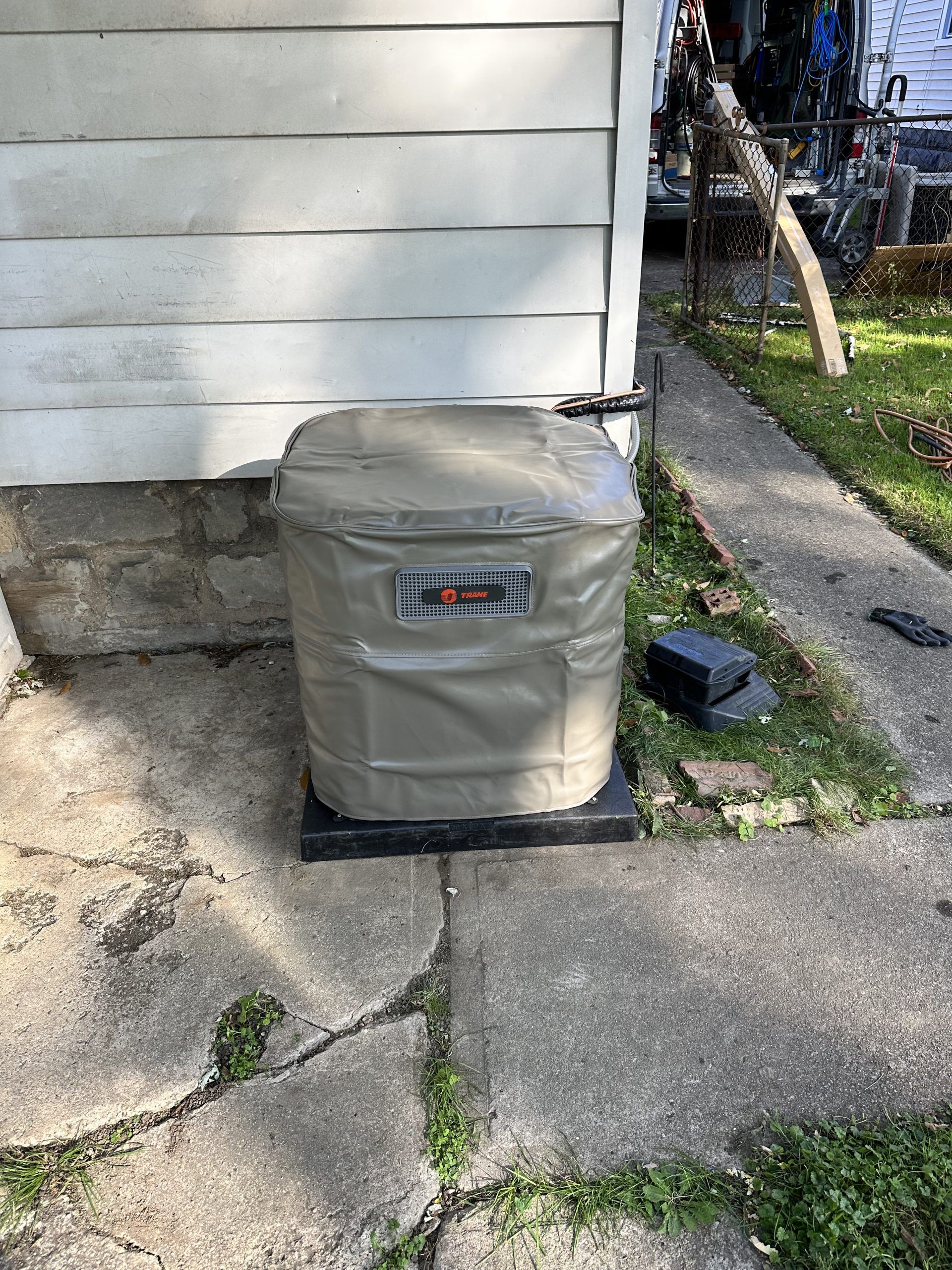 Generator covered in a beige protective cover, placed on a black platform next to a concrete wall.