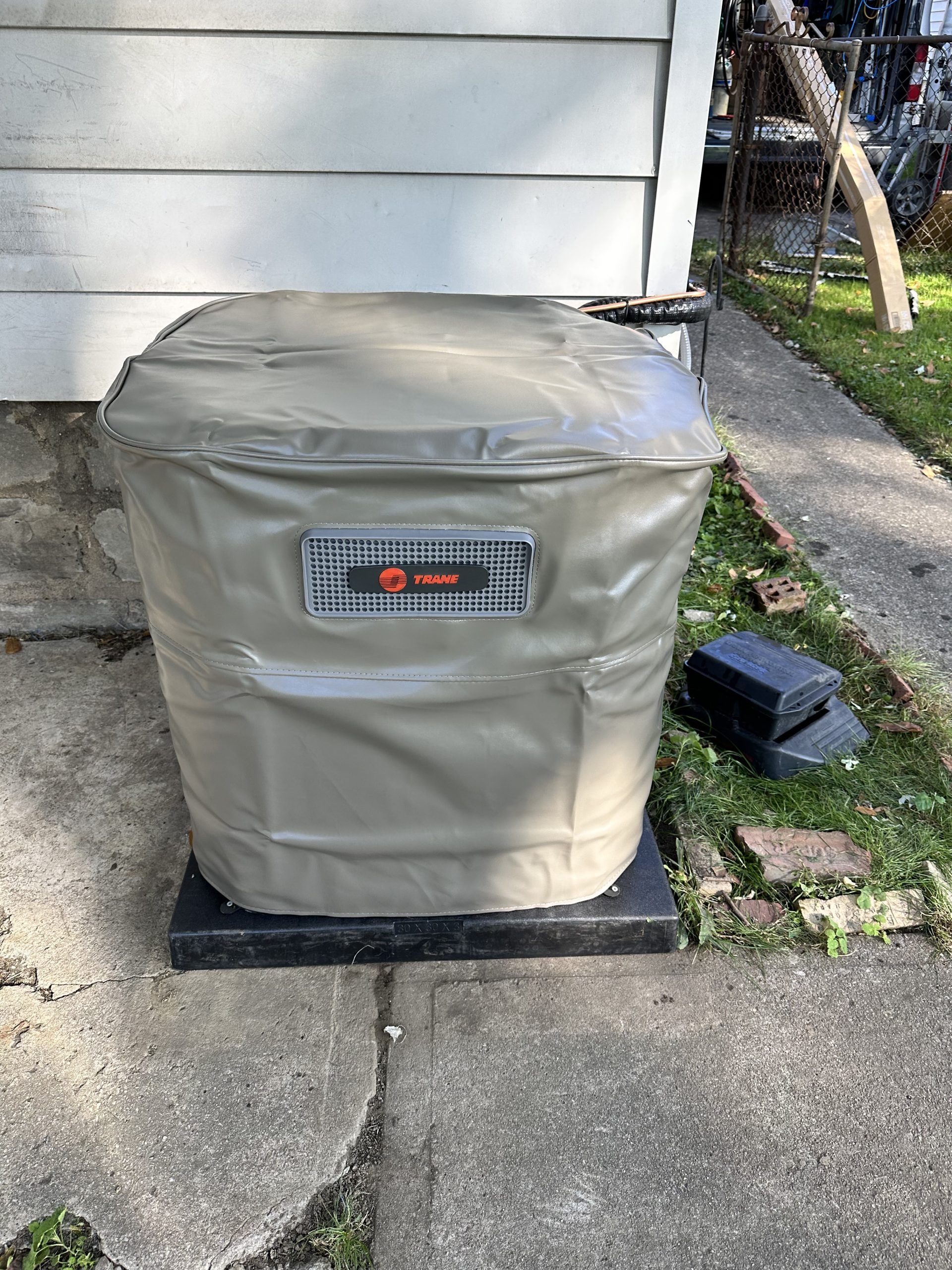 Tan generator covered with a tan cover sits on a black platform next to a house.