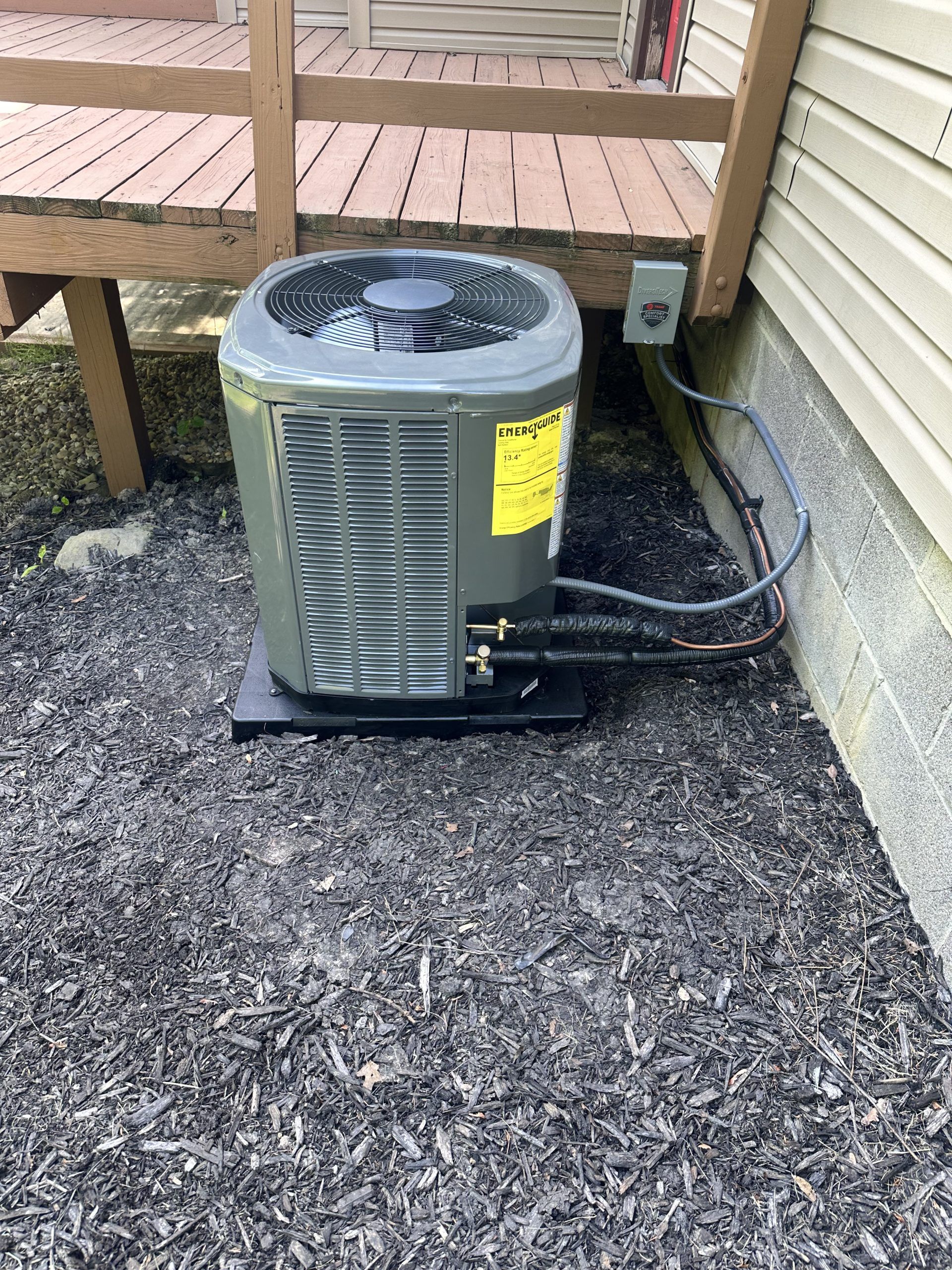 An air conditioning unit on a black platform next to a house with black mulch.
