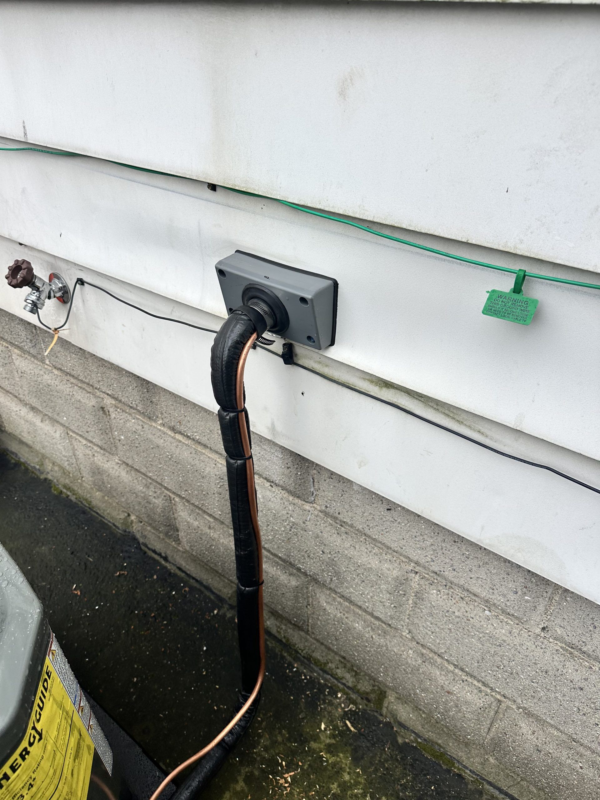 Electrical conduit exiting a gray box on a white house exterior with copper piping below.