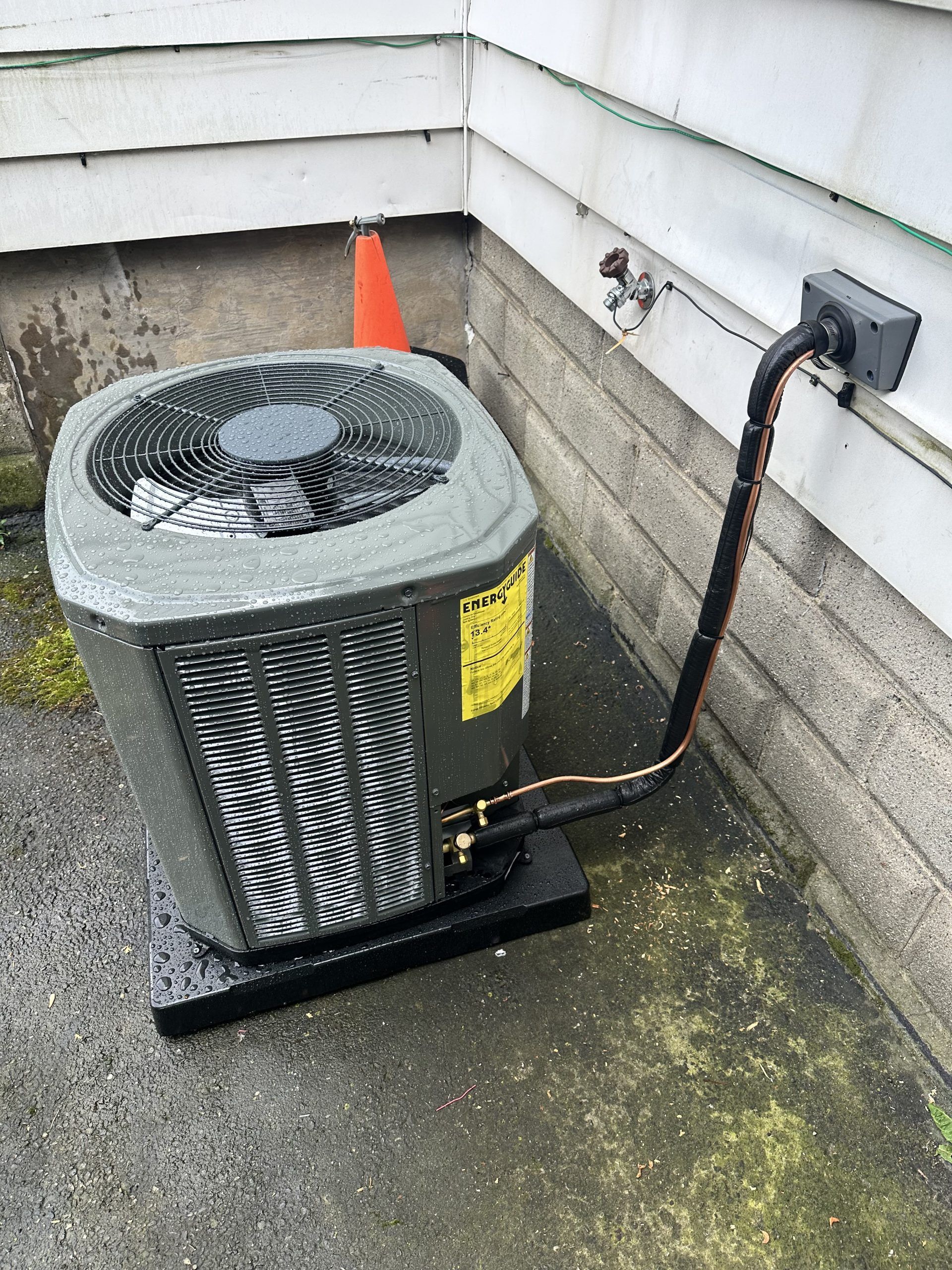 Air conditioning unit on a black base next to a white wall, copper tubing connecting to electrical box.