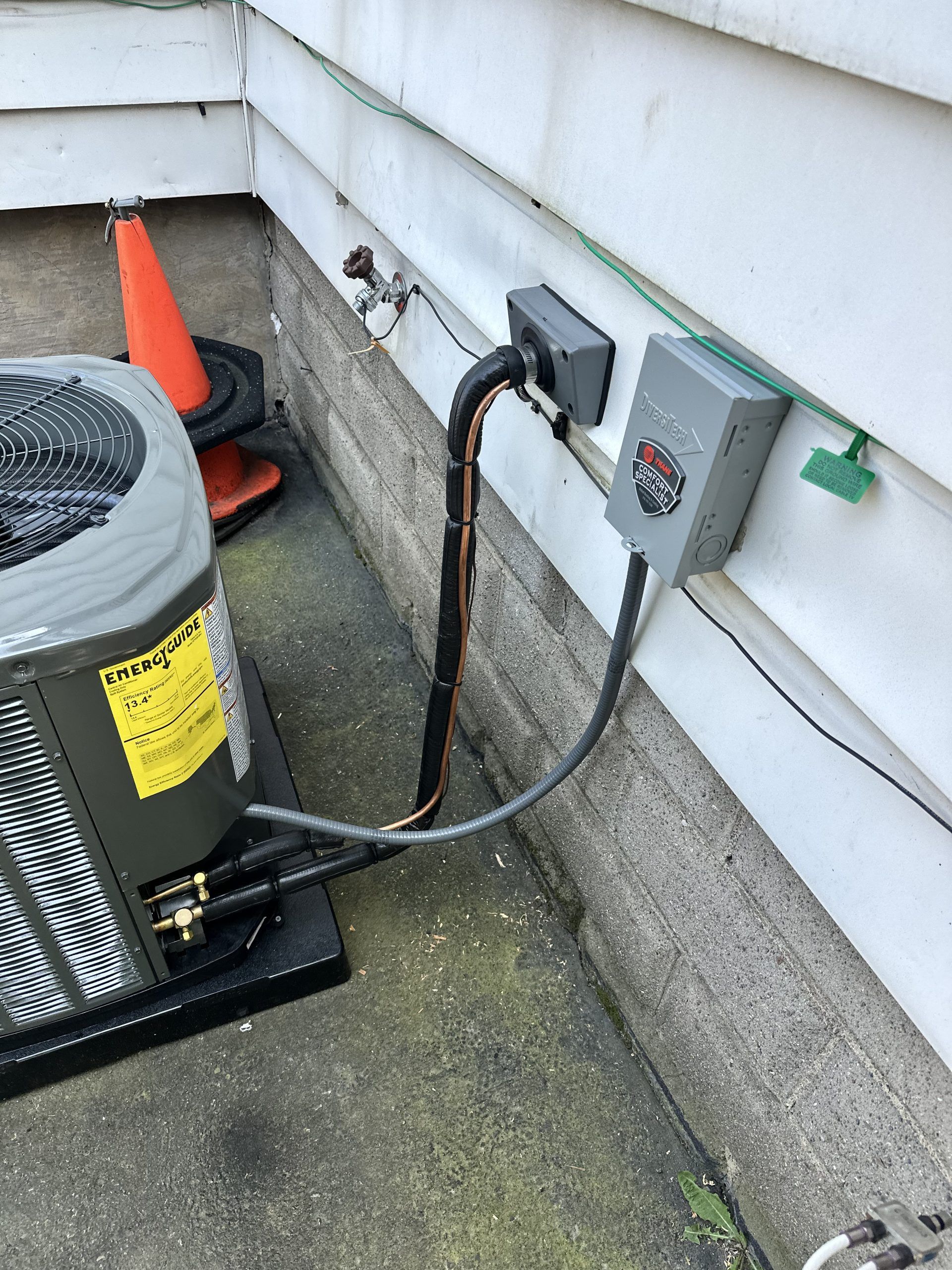 An air conditioning unit next to a building with electrical boxes and piping.