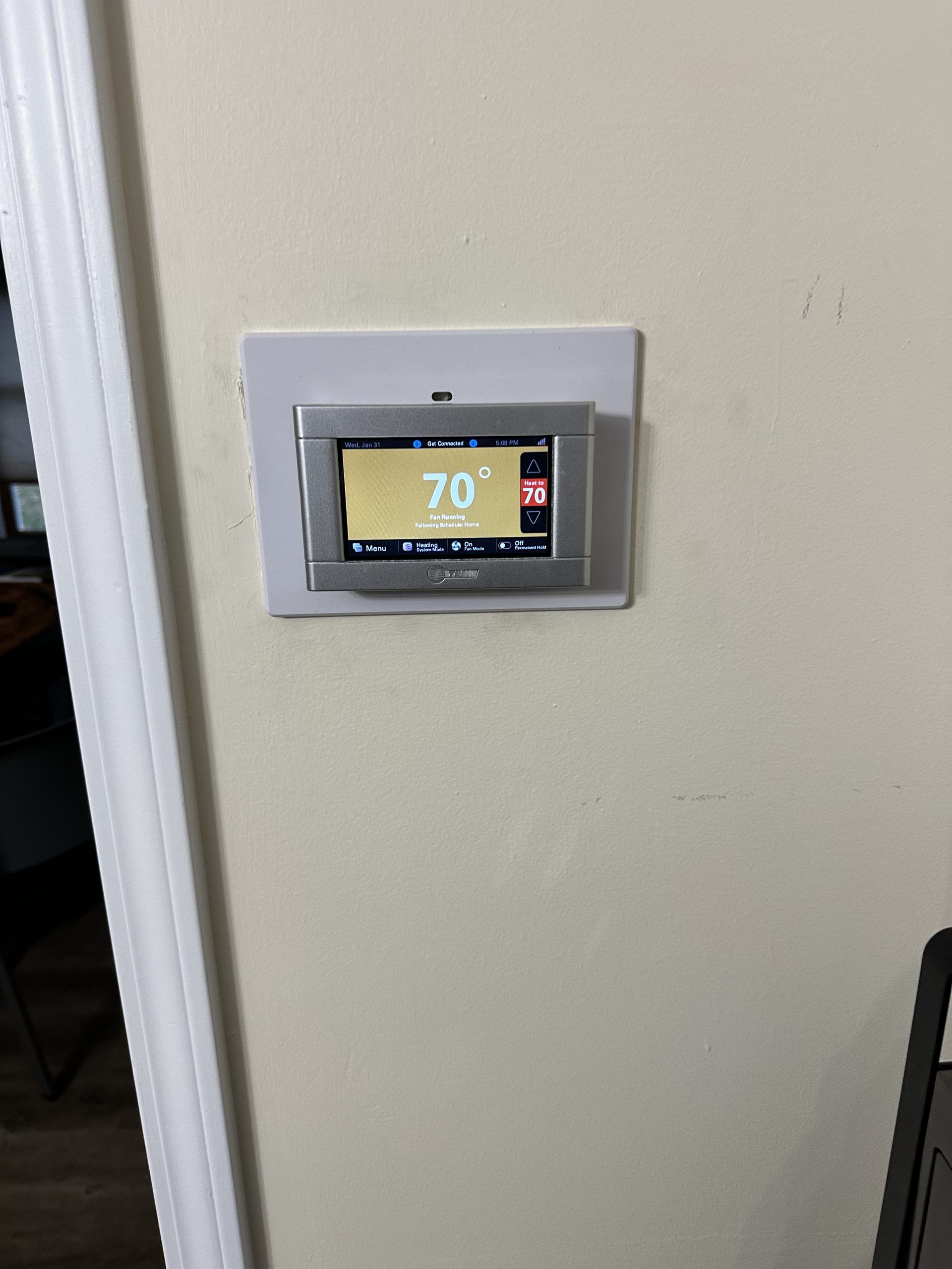 Thermostat on a light-colored wall, displaying 70 degrees. Silver trim, light tan background.