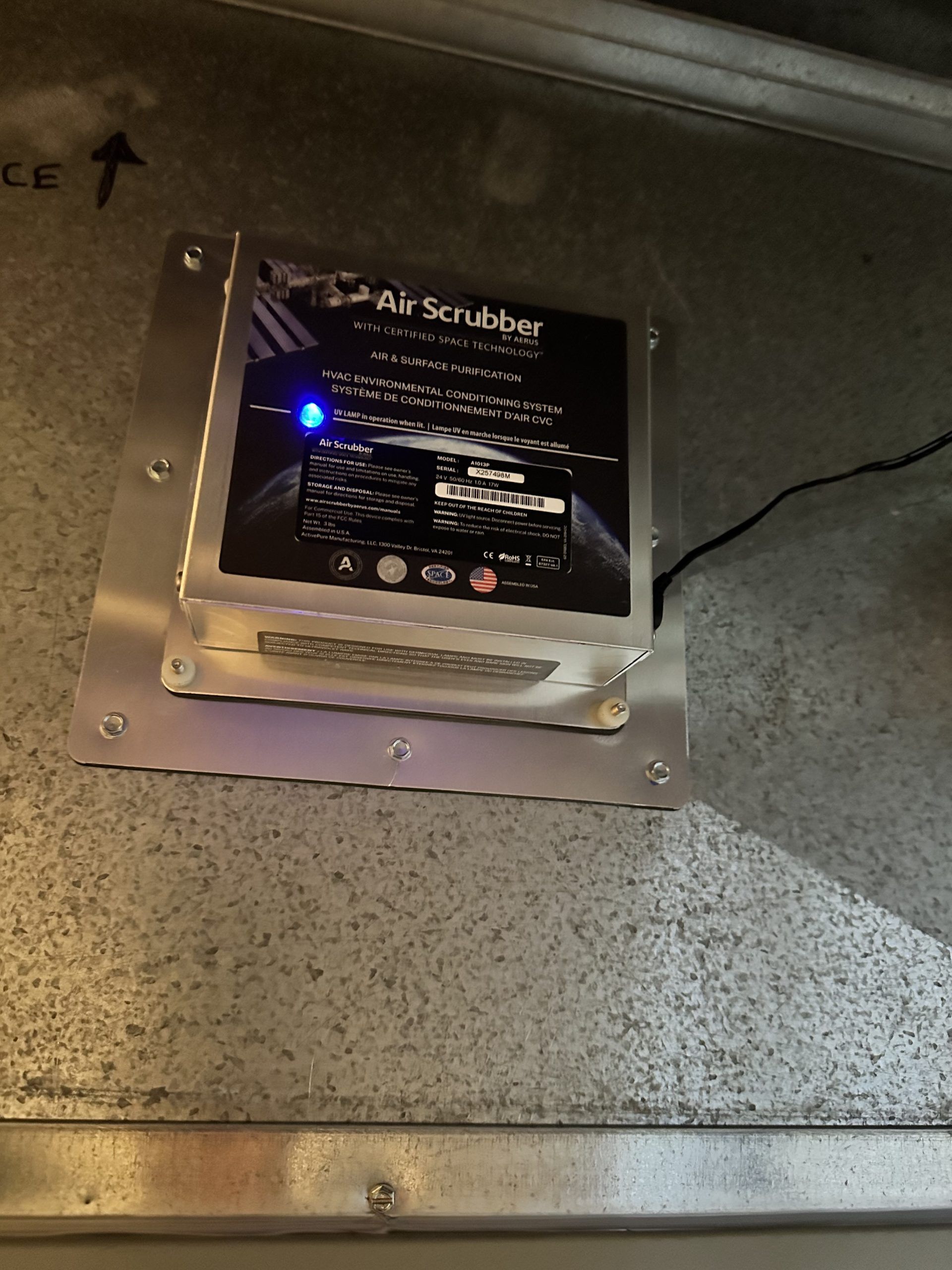 Air Scrubber device installed in a metal air duct, with a blue light lit up.