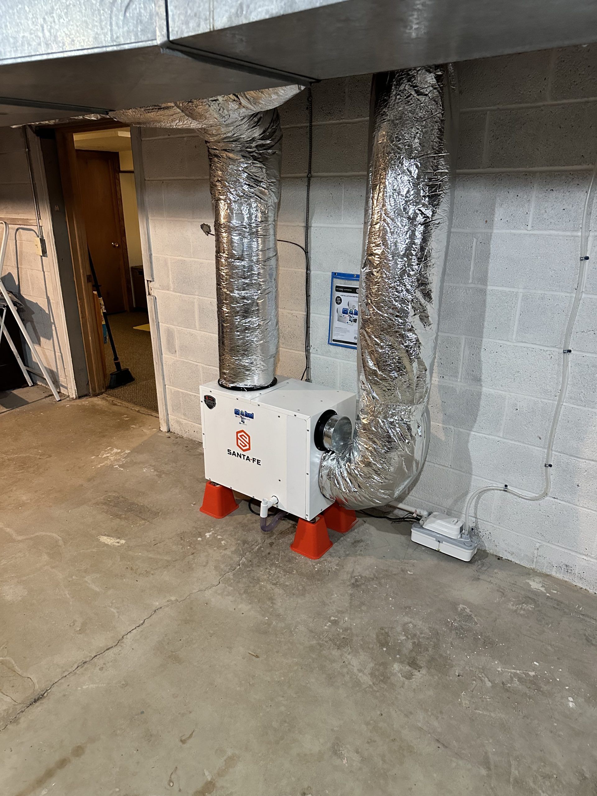 White air purifier with silver ductwork, placed in a concrete basement.