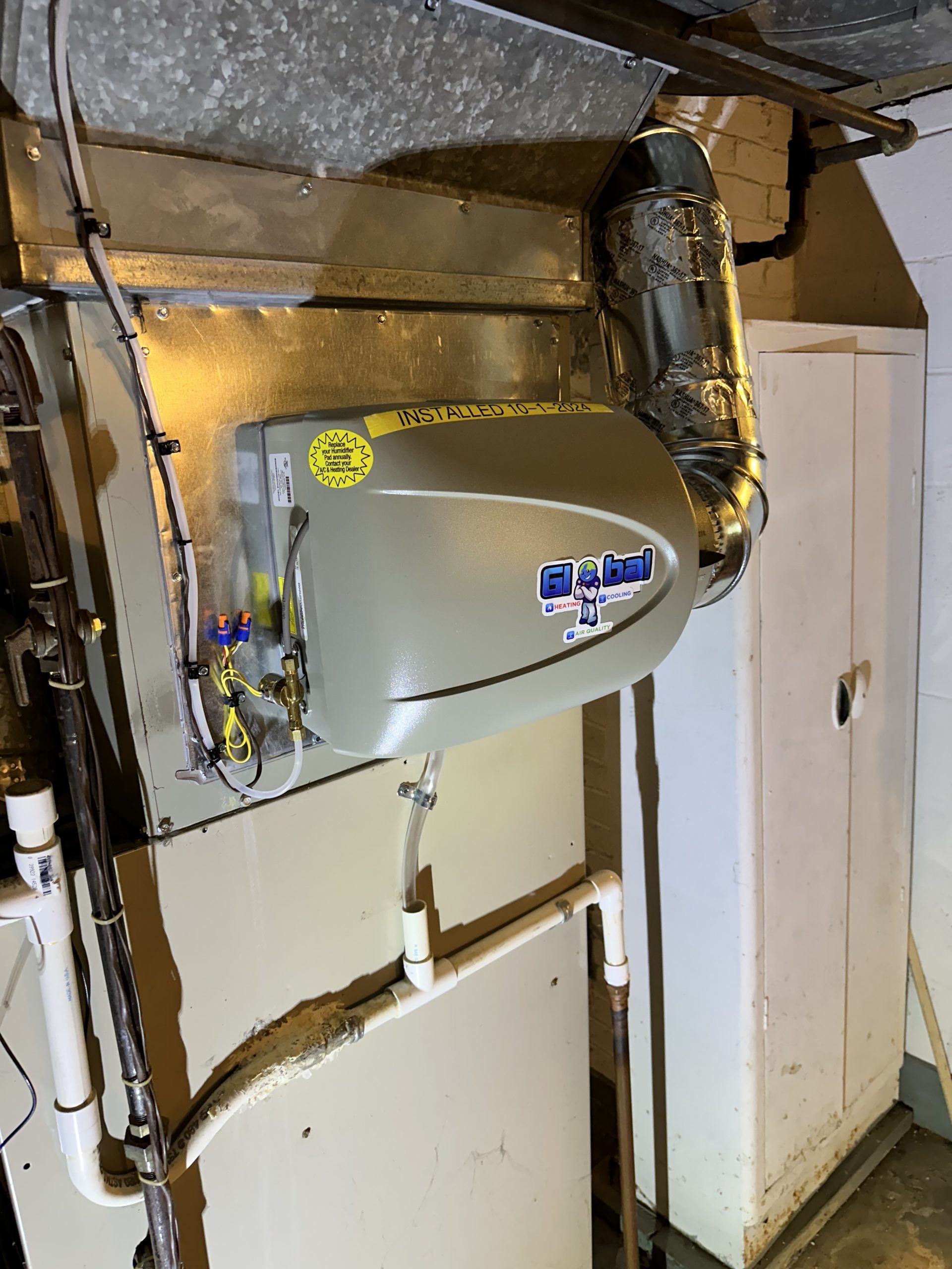 Furnace unit mounted on a wall in a basement, with ductwork and plumbing visible.