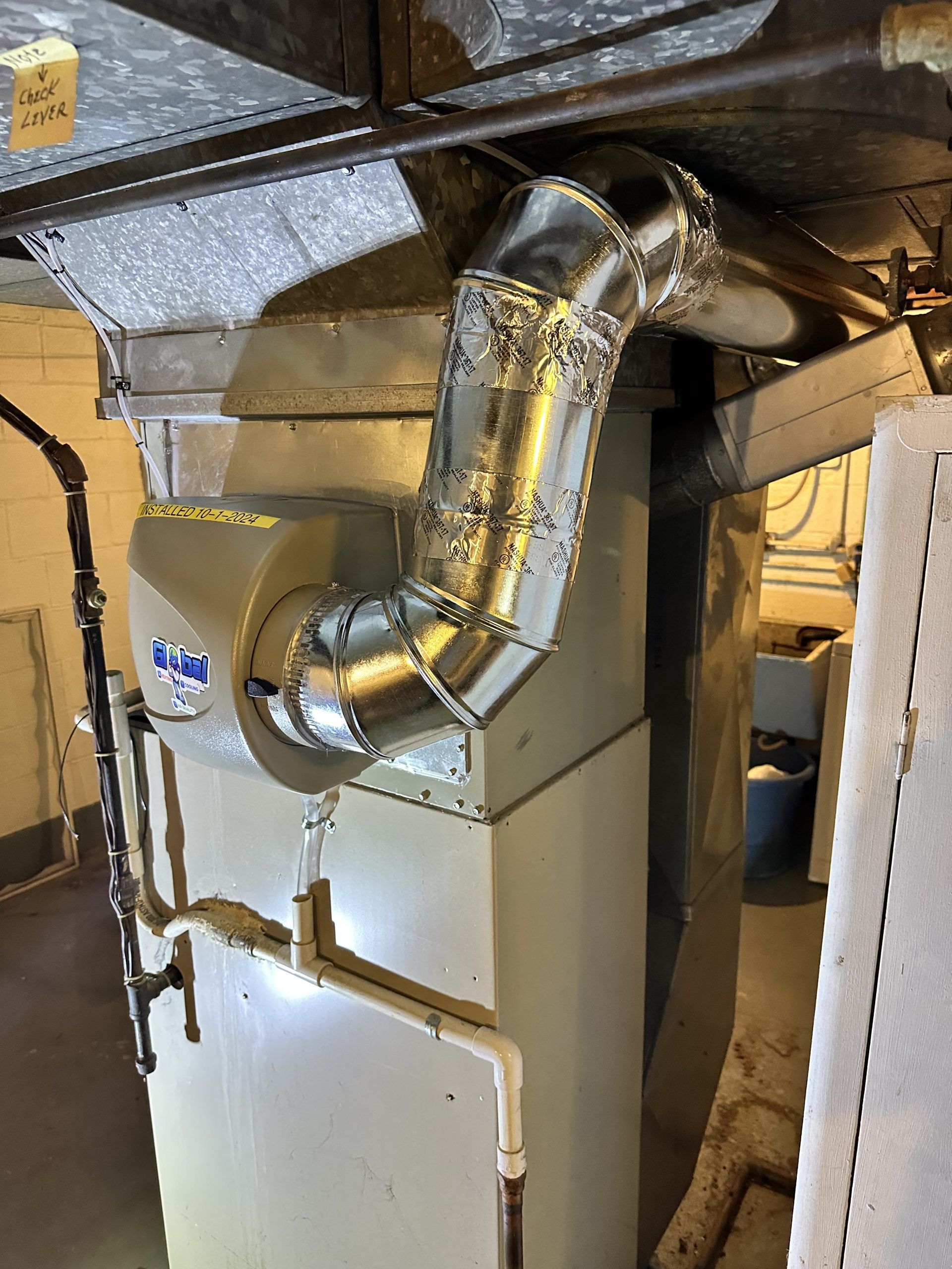 Furnace with ductwork in a basement setting. Gray metal unit with silver and insulated ductwork.