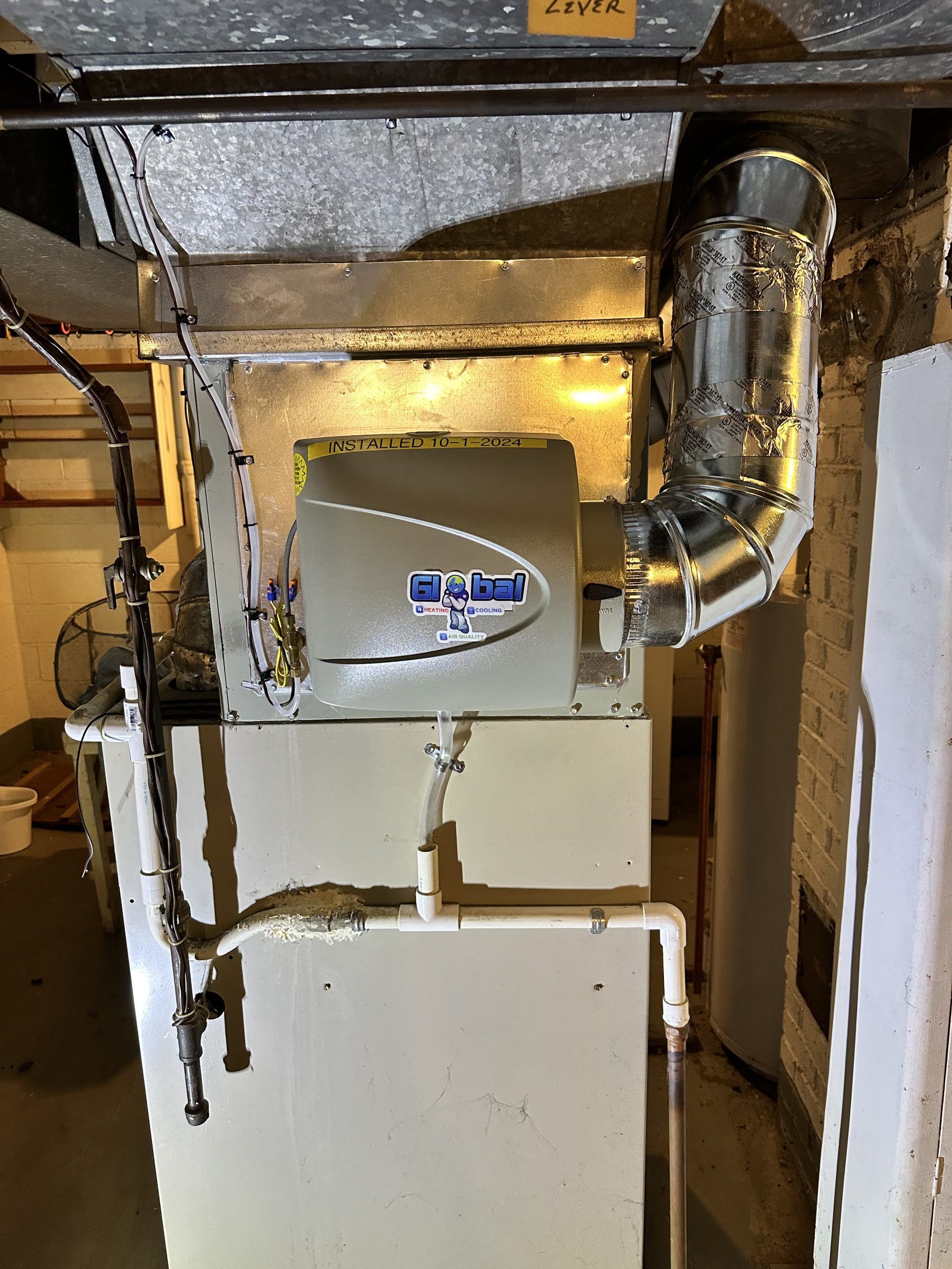A furnace with an attached humidifier in a basement setting.