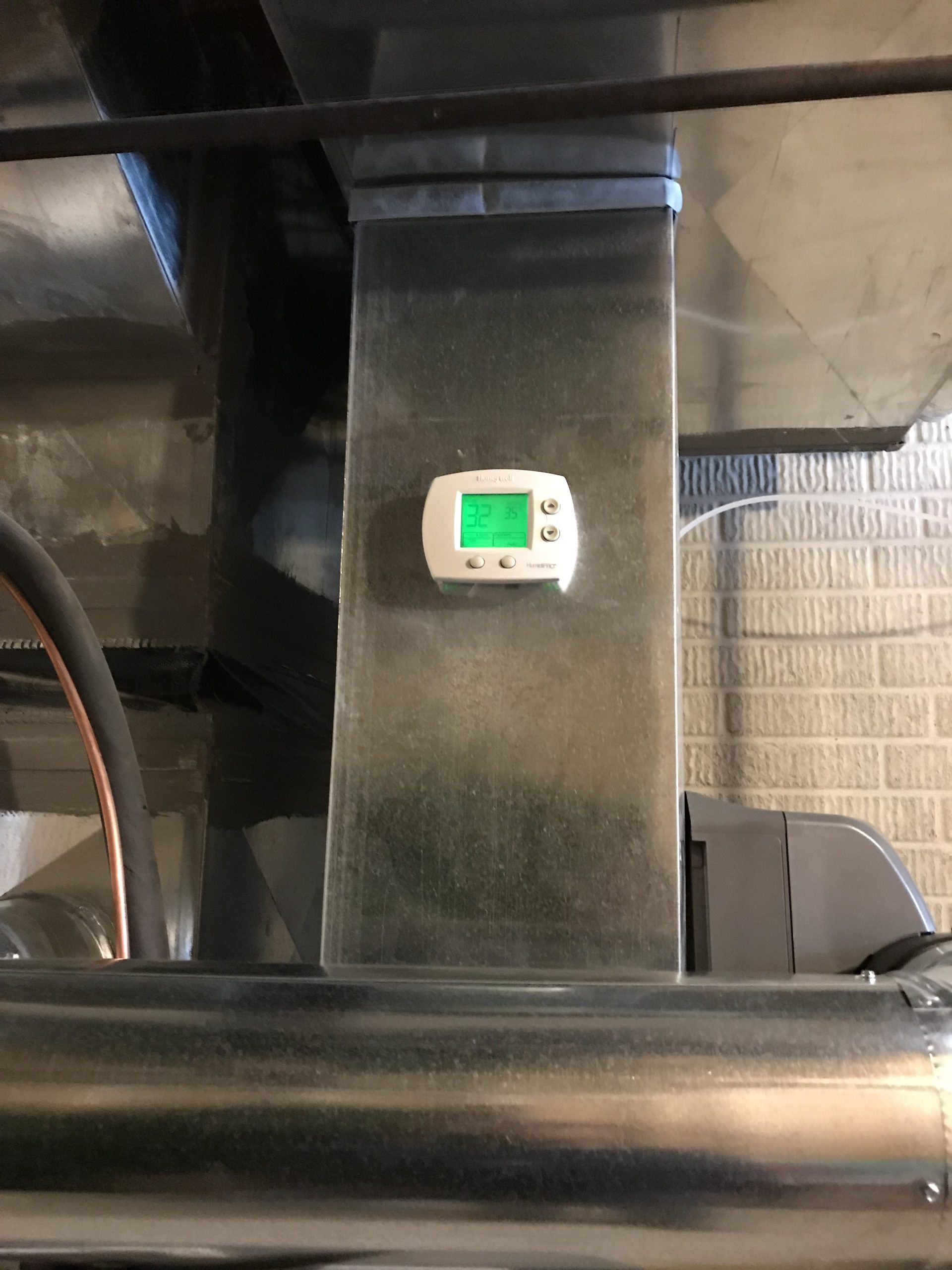 Thermostat mounted on a metal duct, displaying a green temperature reading.