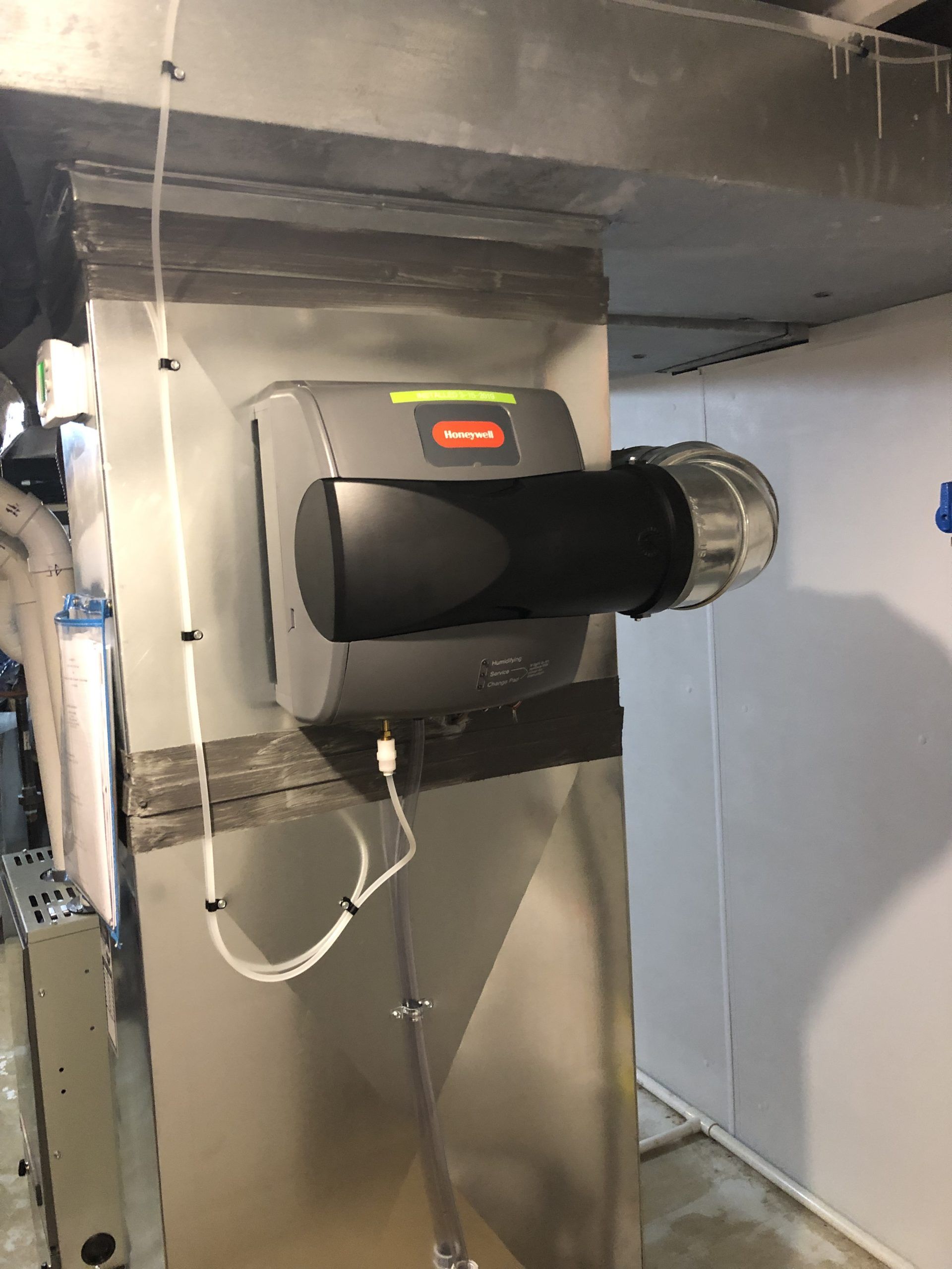 Humidifier attached to HVAC ductwork, gray and black, in a basement.
