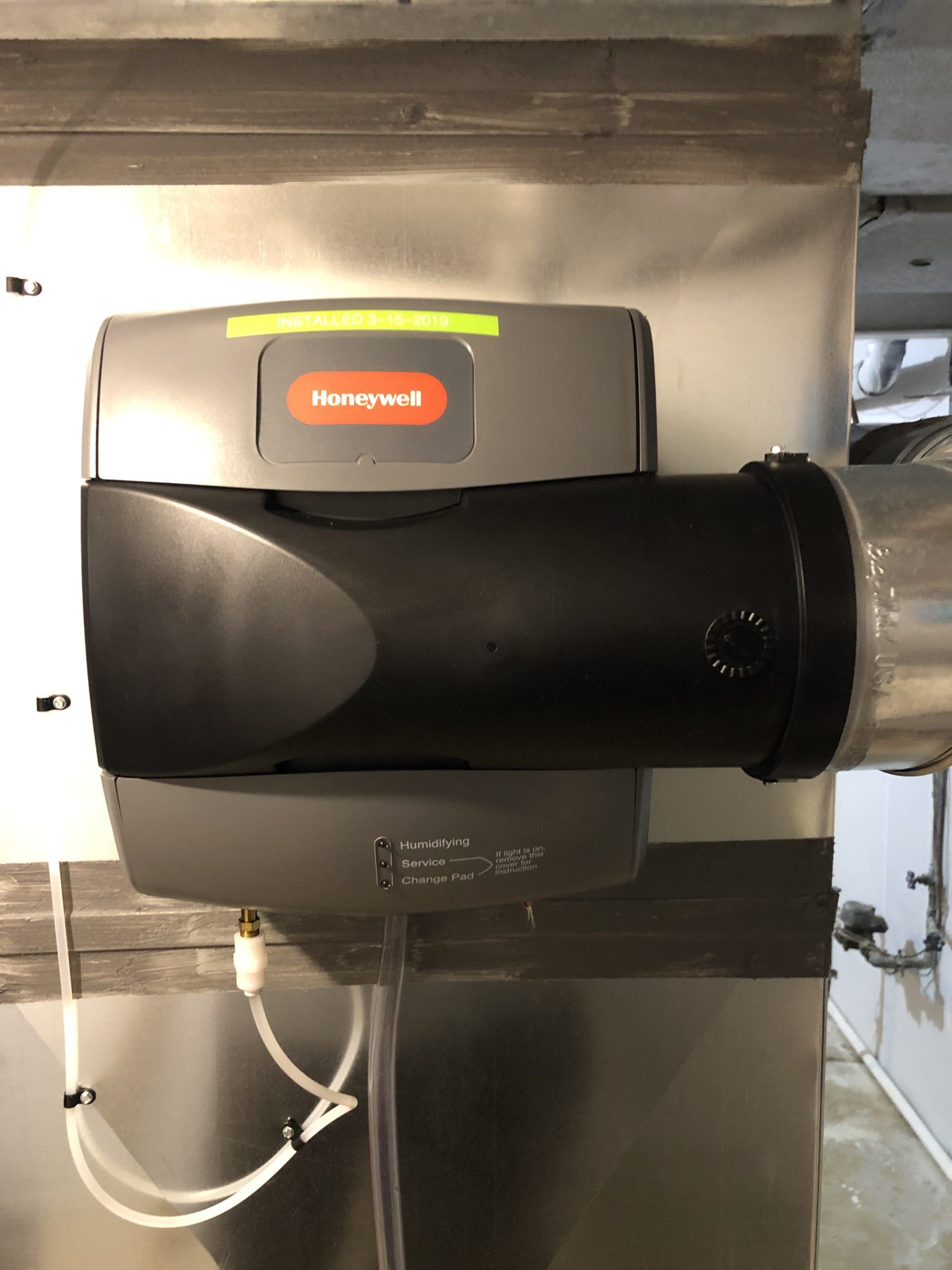 Honeywell humidifier attached to ductwork. Gray and black, with a green/red indicator light.