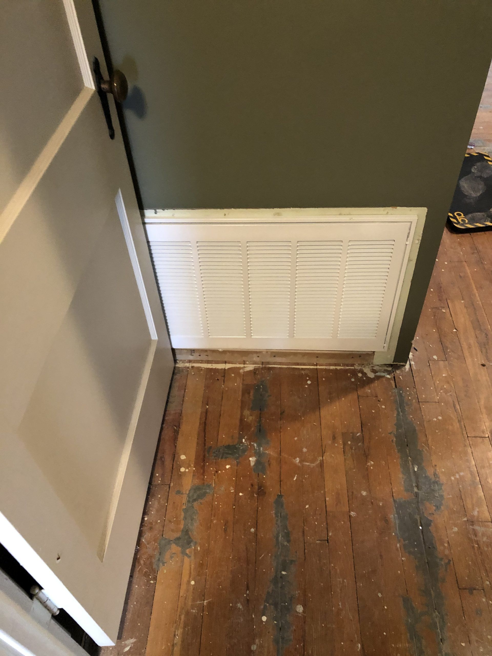 Open doorway with white air vent in a green wall. Wood floor with paint spills.