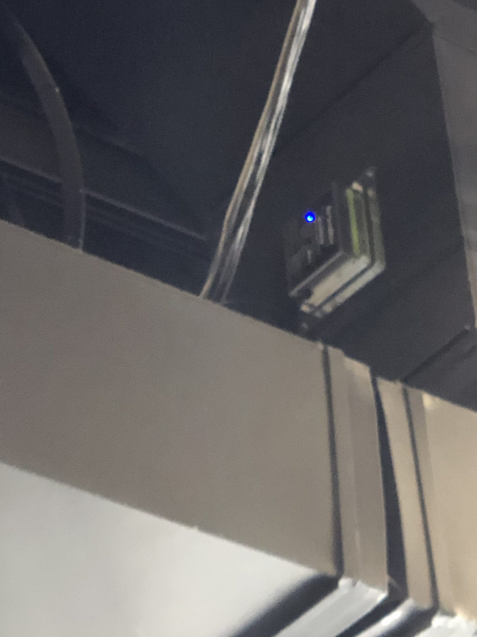 Small electronic device with a blue light mounted on a ceiling beam with wires.
