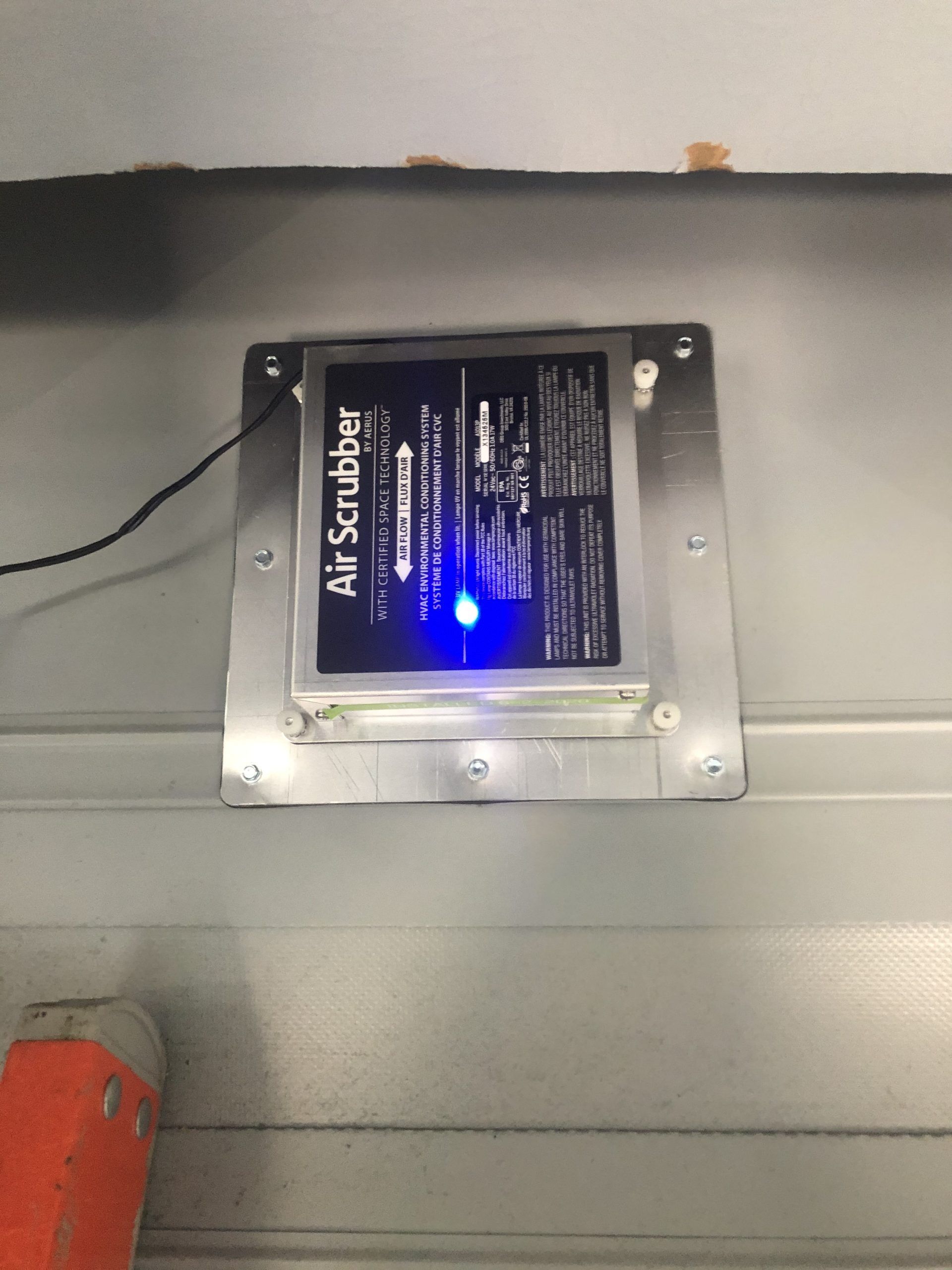 Air Scrubber device with a blue light mounted on a gray wall.