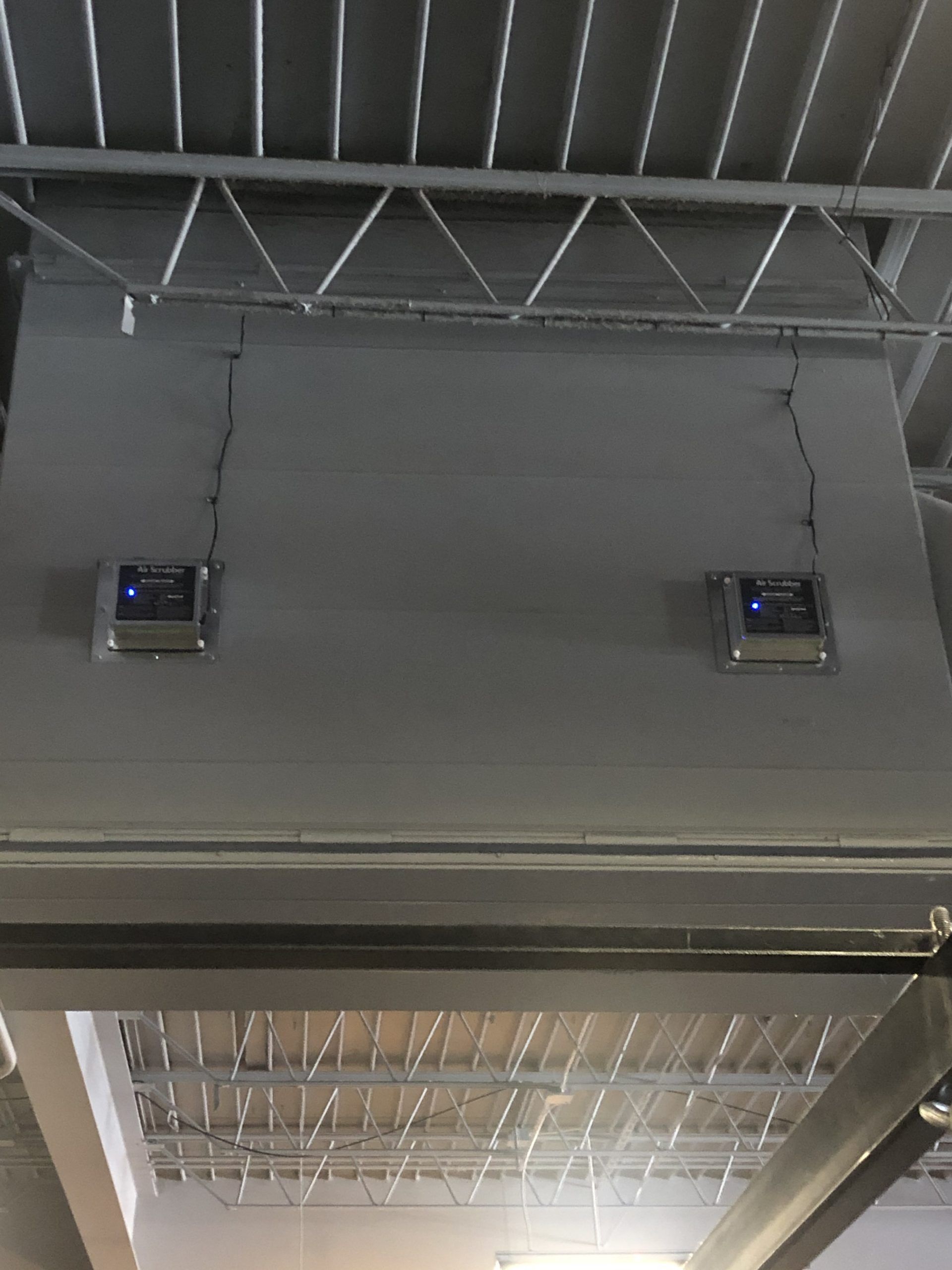 Two gray control panels mounted on a gray wall under a metal ceiling. Wires run to the panels.