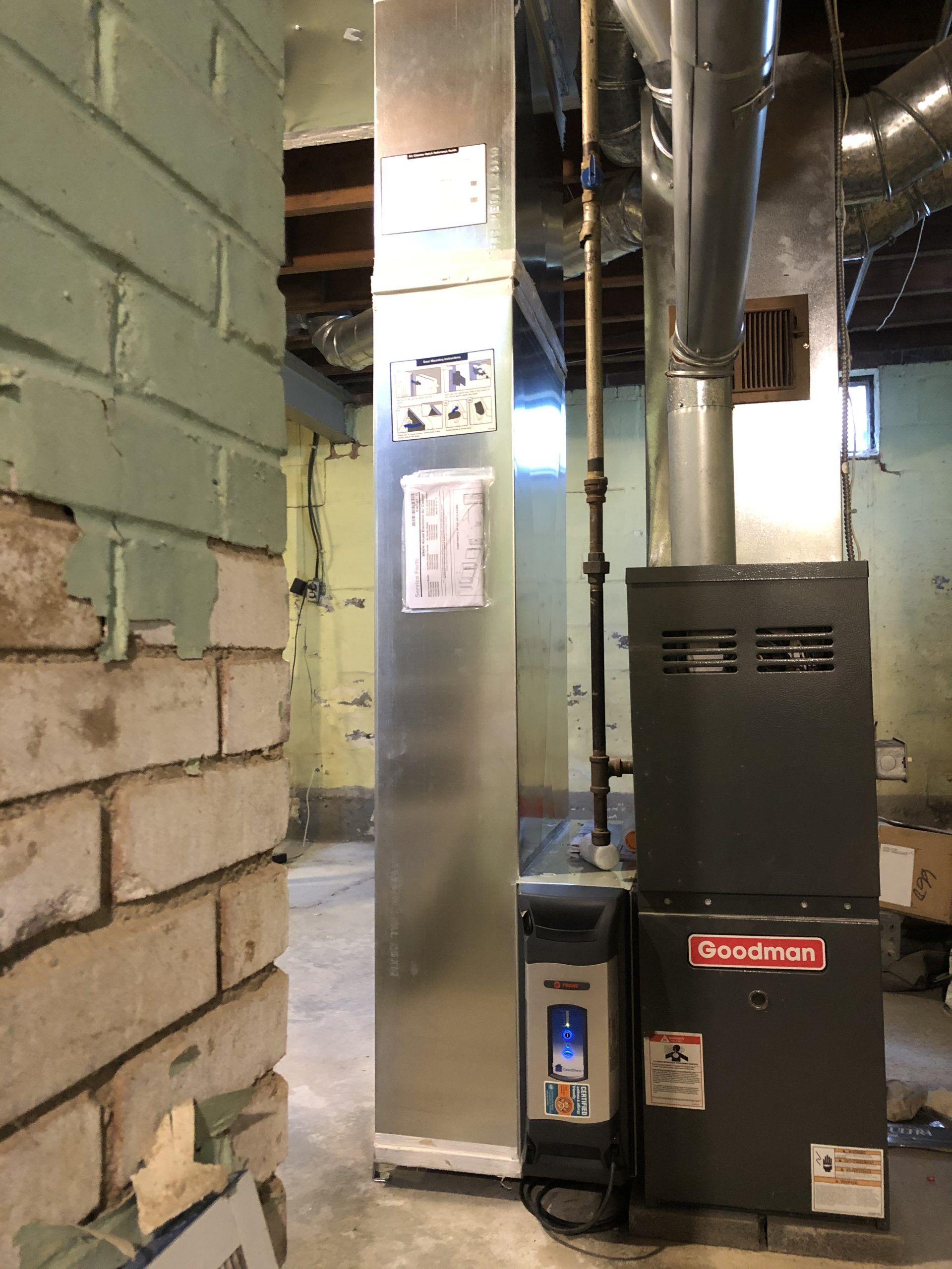 Furnace in a basement next to a brick wall. Silver ductwork runs above.