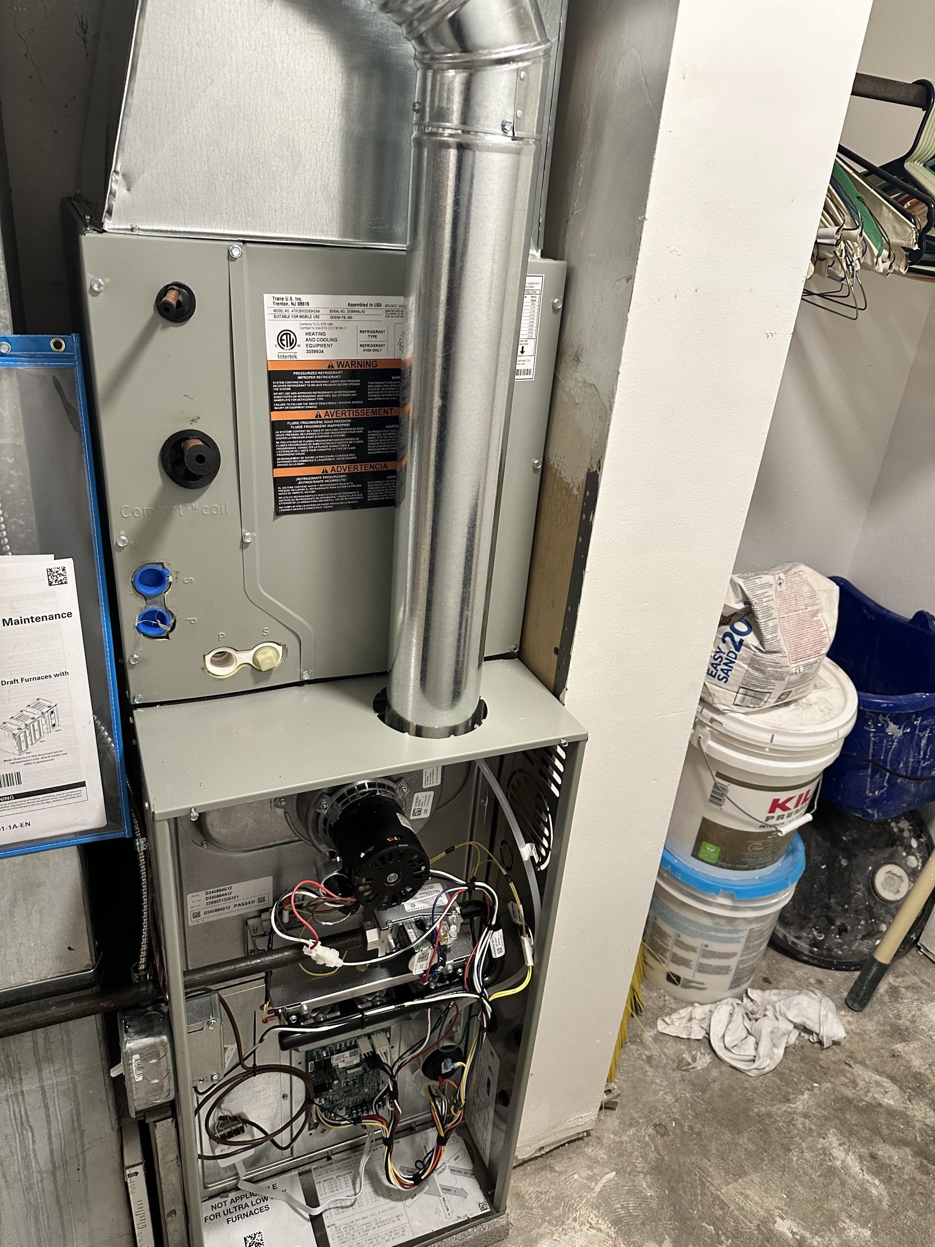 Furnace unit with a vent pipe and visible interior components. Located near buckets and a wall.