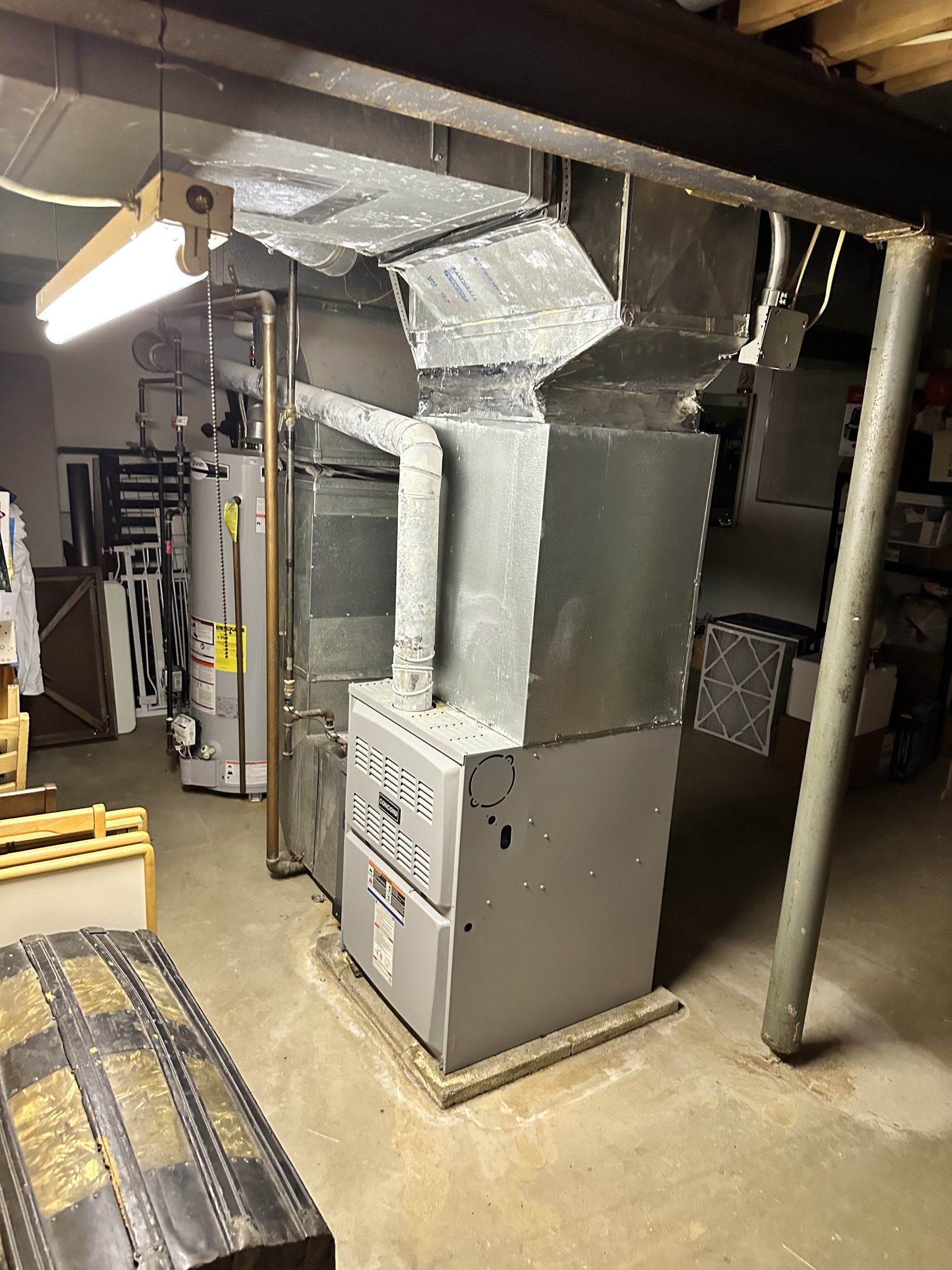 Furnace and ductwork in a basement. Metal, gray appliance. Fluorescent light overhead.