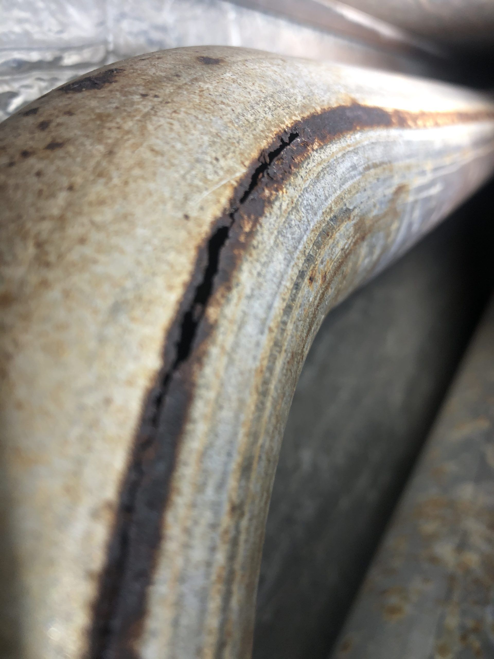 Close-up of a bent, rusty metal pipe with a prominent, dark crack running along its surface.
