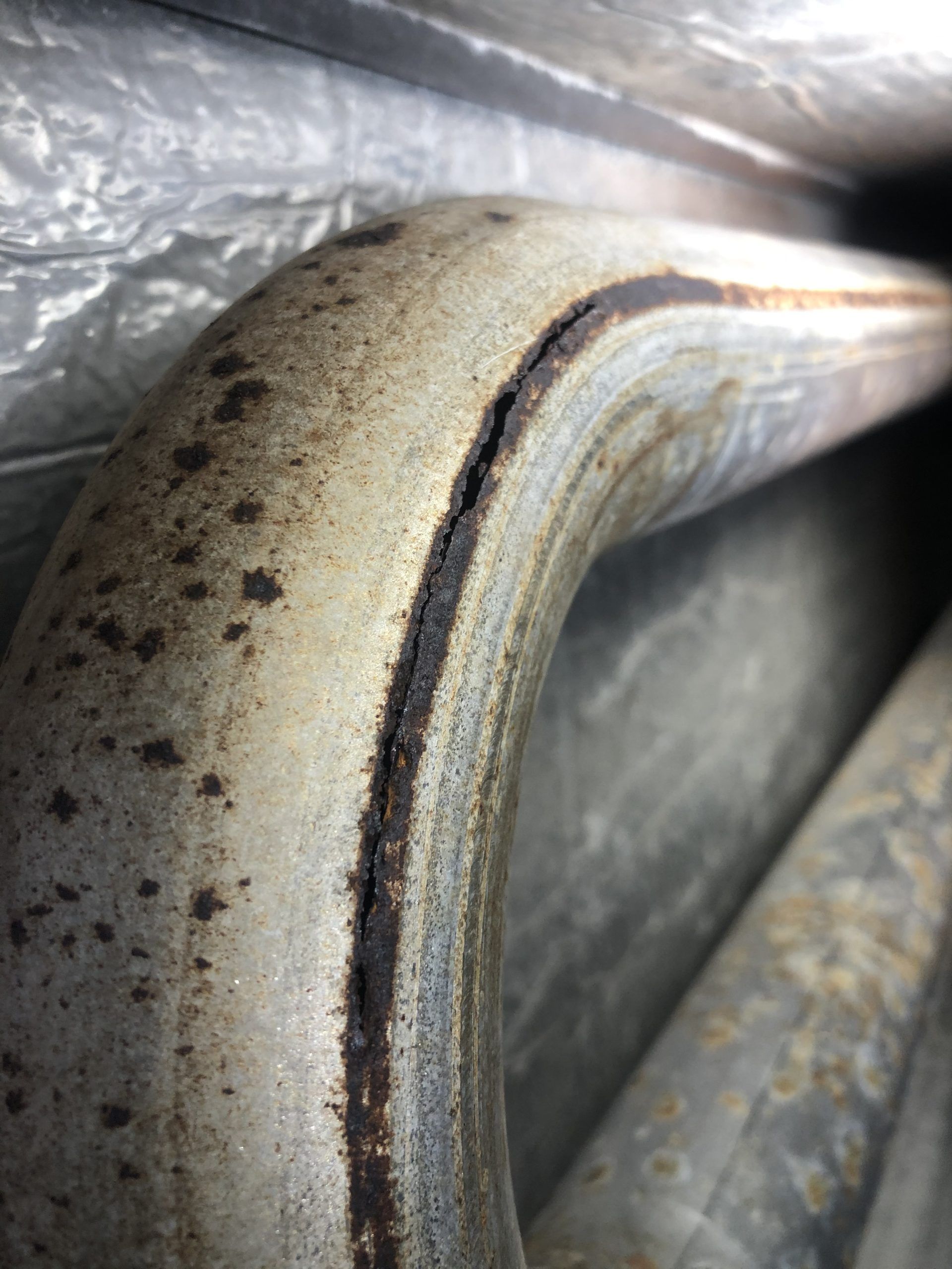Bent metal pipe section with a long, dark split, showing rust and discoloration.