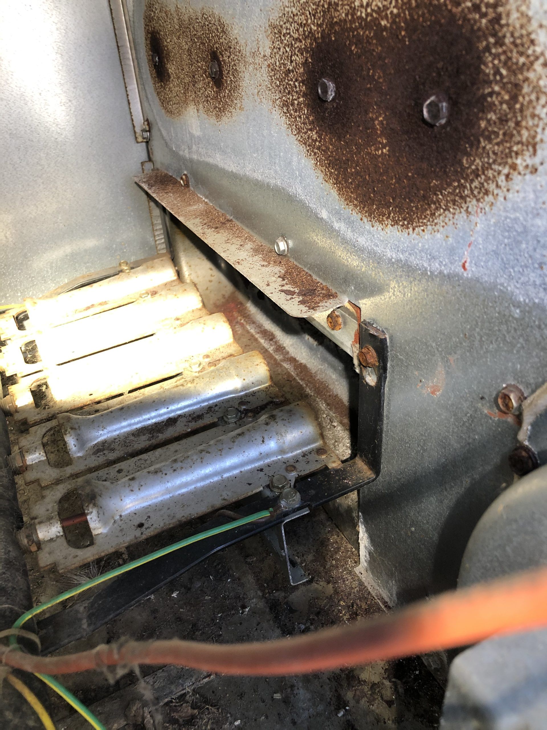 Close-up of rusty metal components inside a machine. Two silver tubes are visible below a rusted bracket.