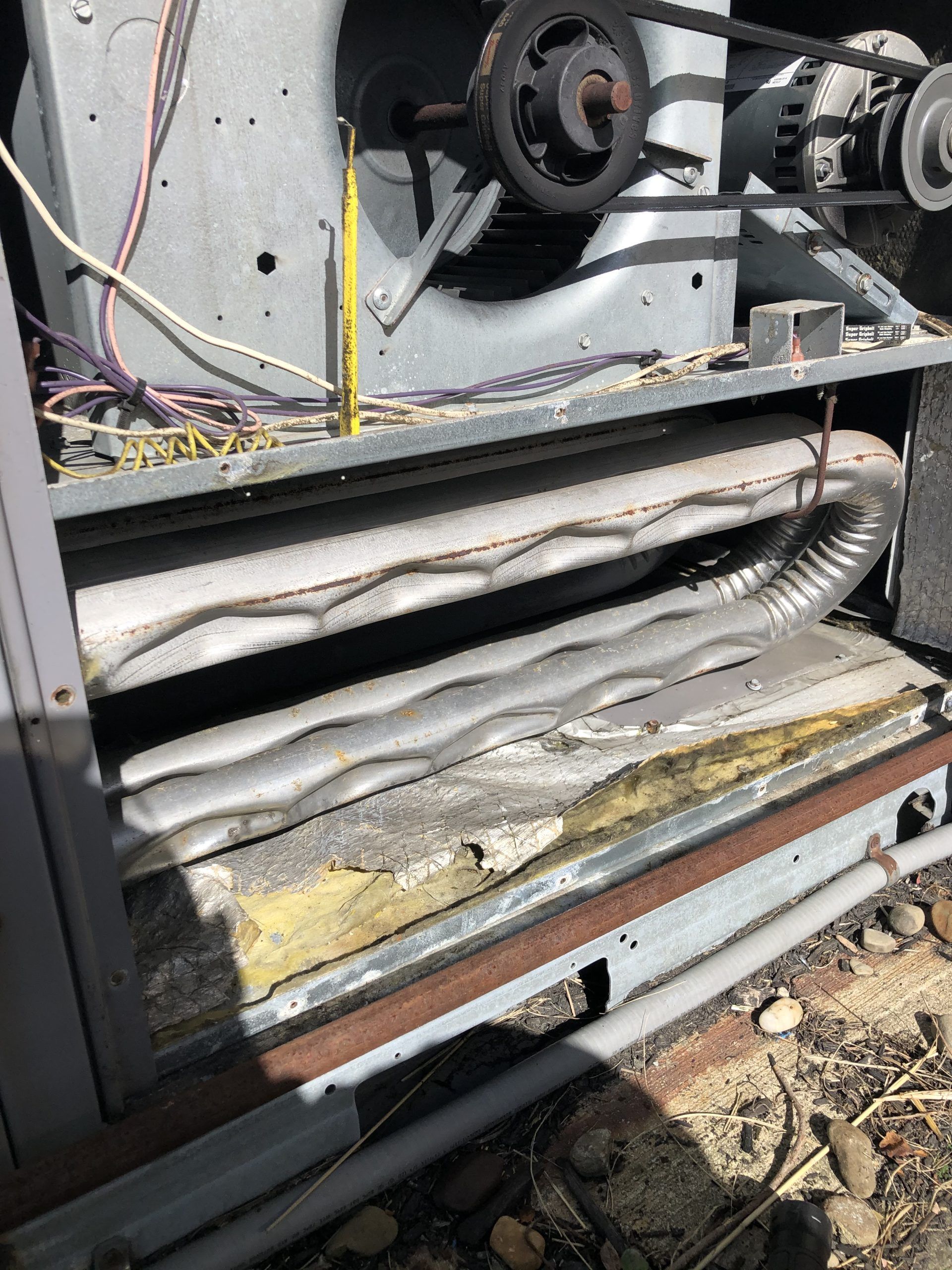 Open air handler unit with a coil, fan, and motor, showing wear and dust.