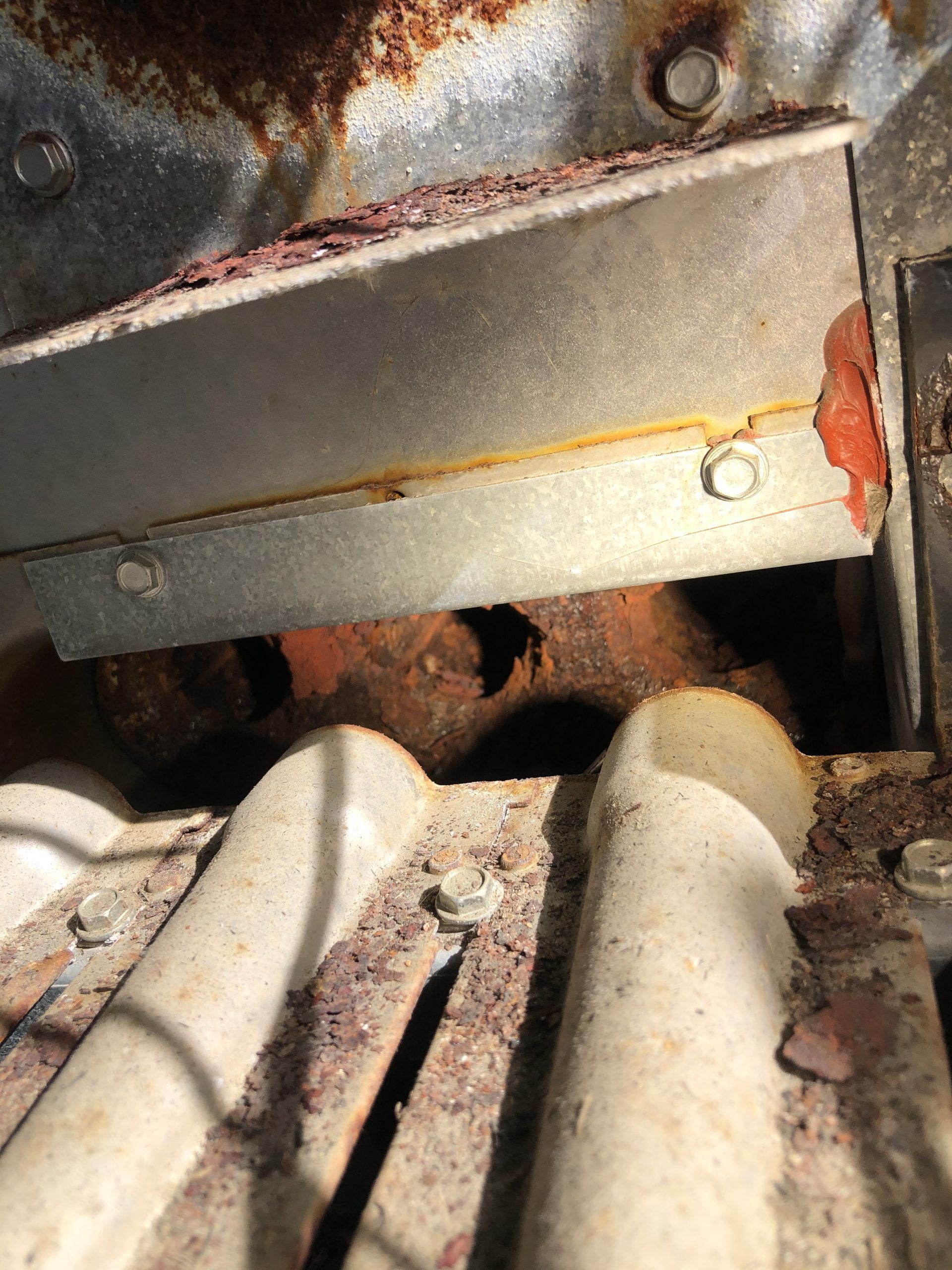 Close-up of a rusted furnace component with a metal cover secured by bolts, displaying signs of corrosion.