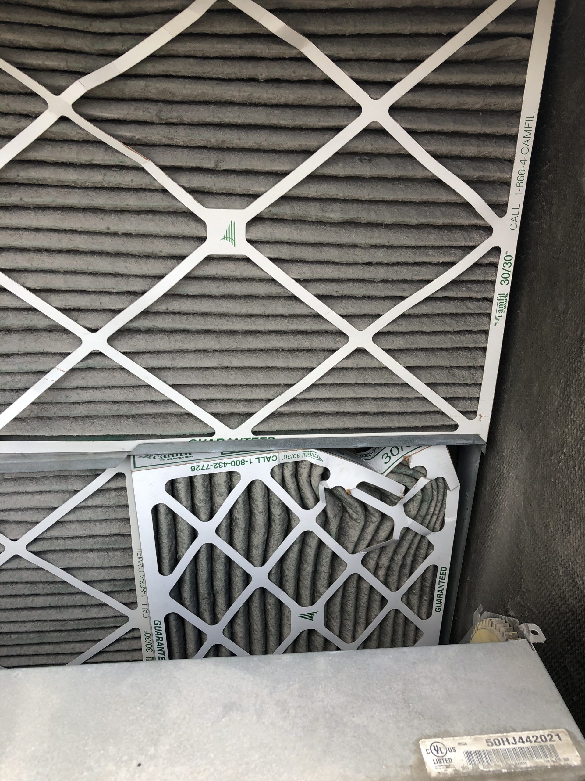 Close-up of two dirty air filters, one partially pulled out, in a metal housing. Gray with collected debris.