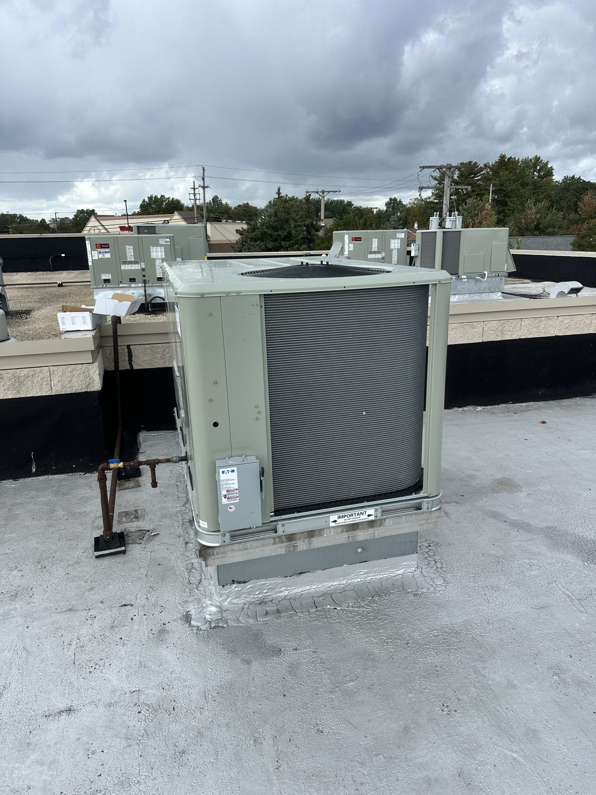 Rooftop air conditioning unit with a metal grill, set against a cloudy sky.