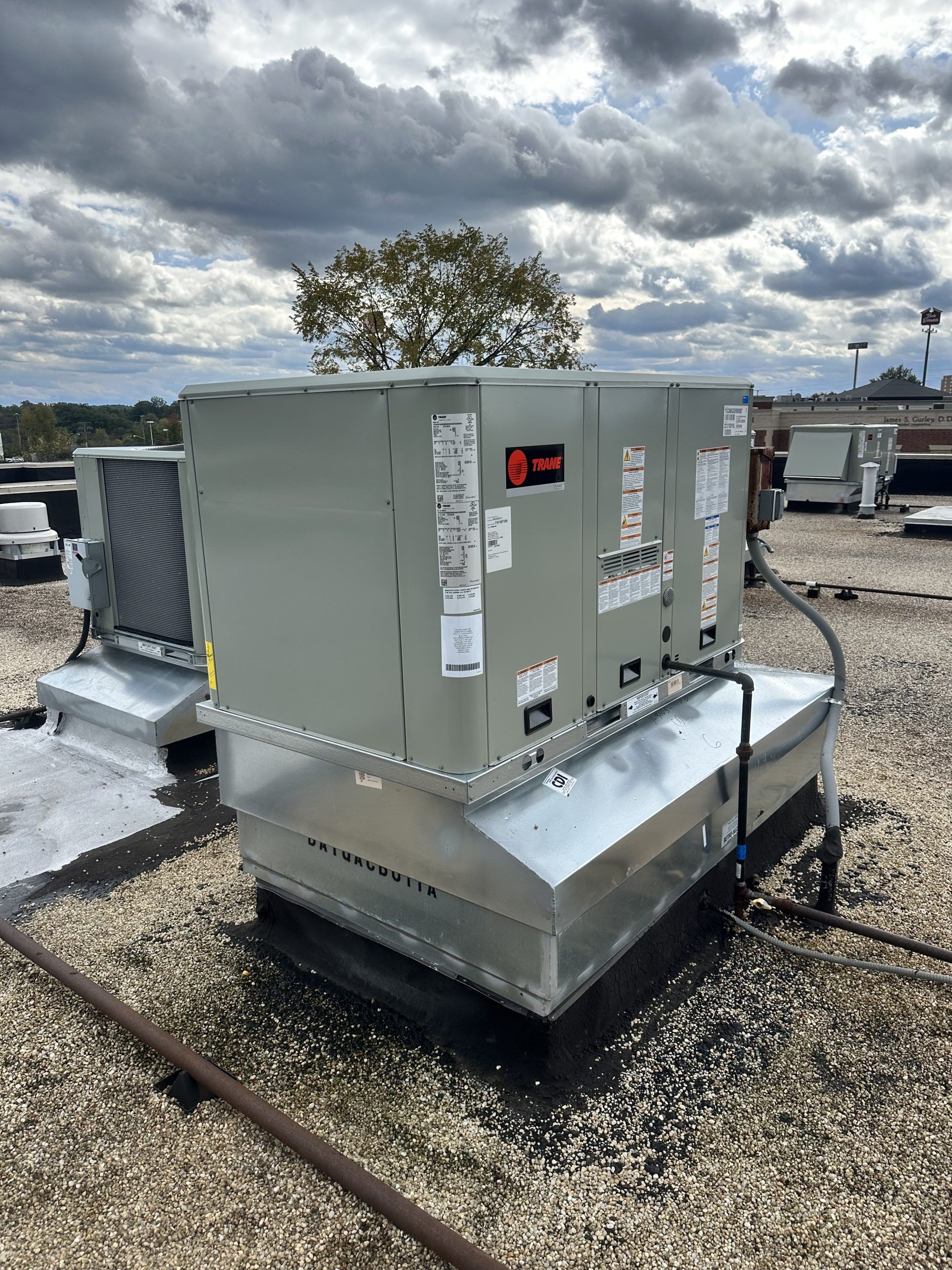 Rooftop HVAC unit, Trane brand, atop a building with a cloudy sky in the background.
